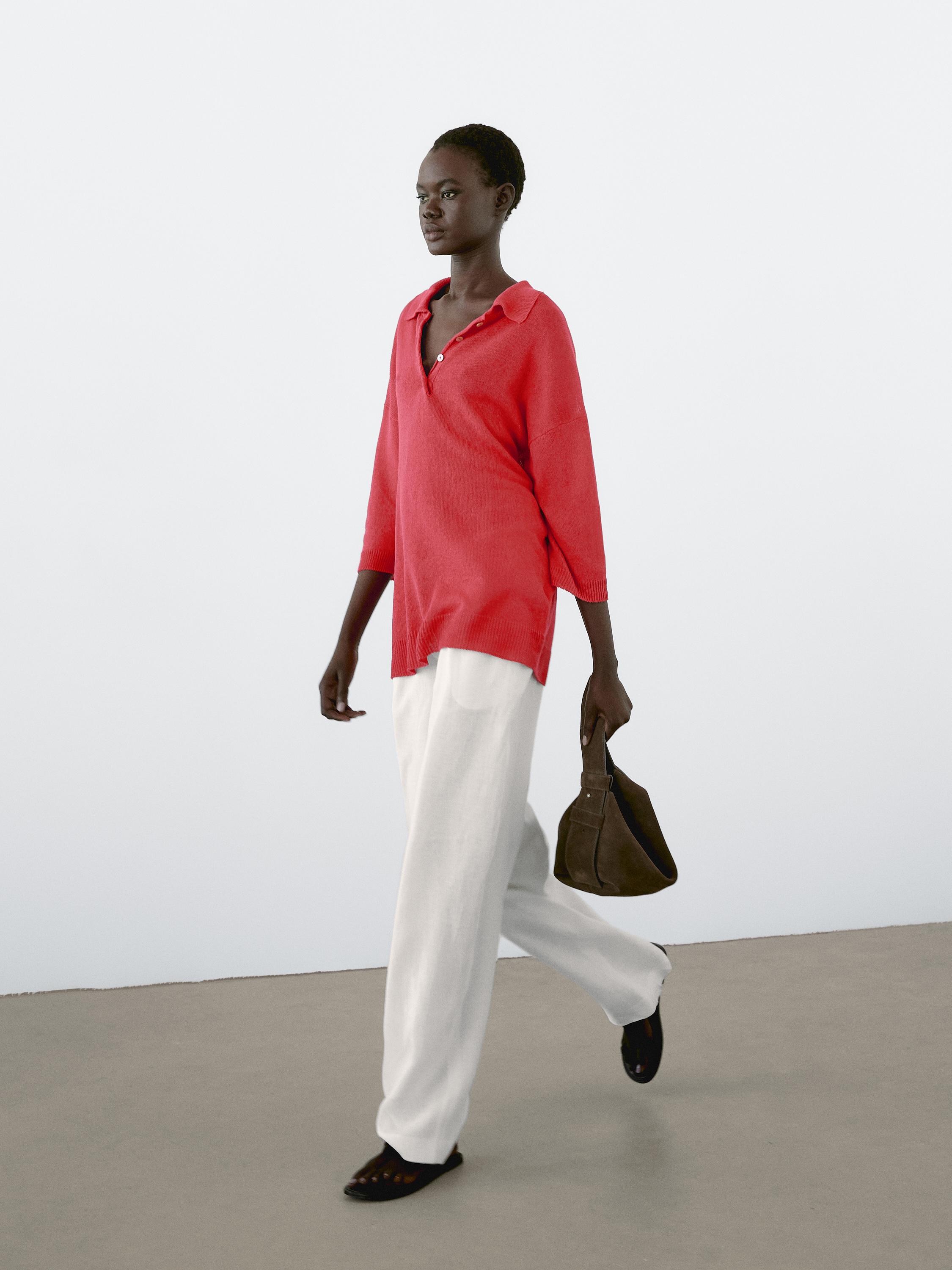 Ensemble composé d'un chemisier rouge à manches trois-quarts et d'un pantalon blanc. Sac à main marron et chaussures noires visibles.