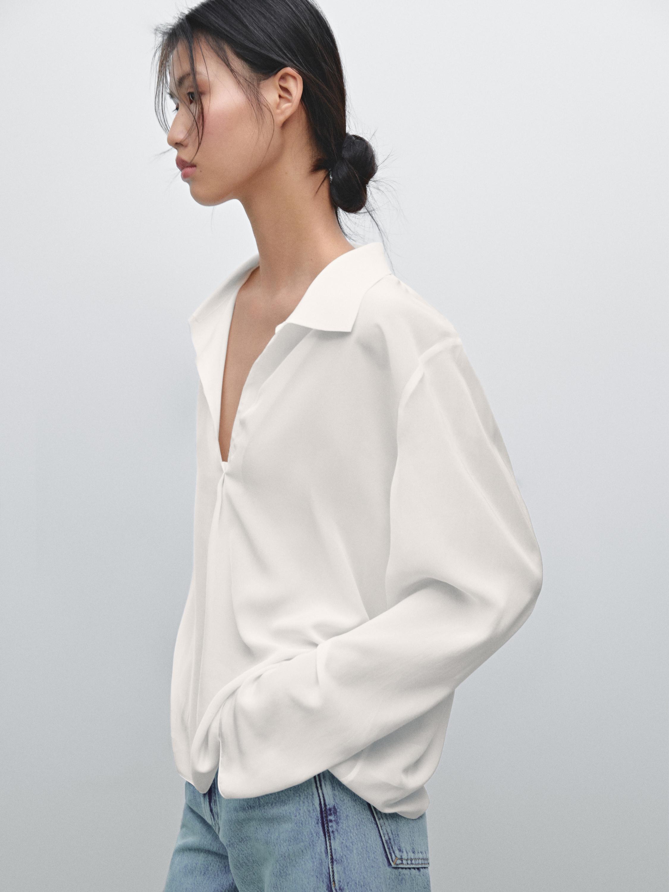 Plan moyen d'une chemise blanche à col ouvert et manches longues, associée à un jean bleu.