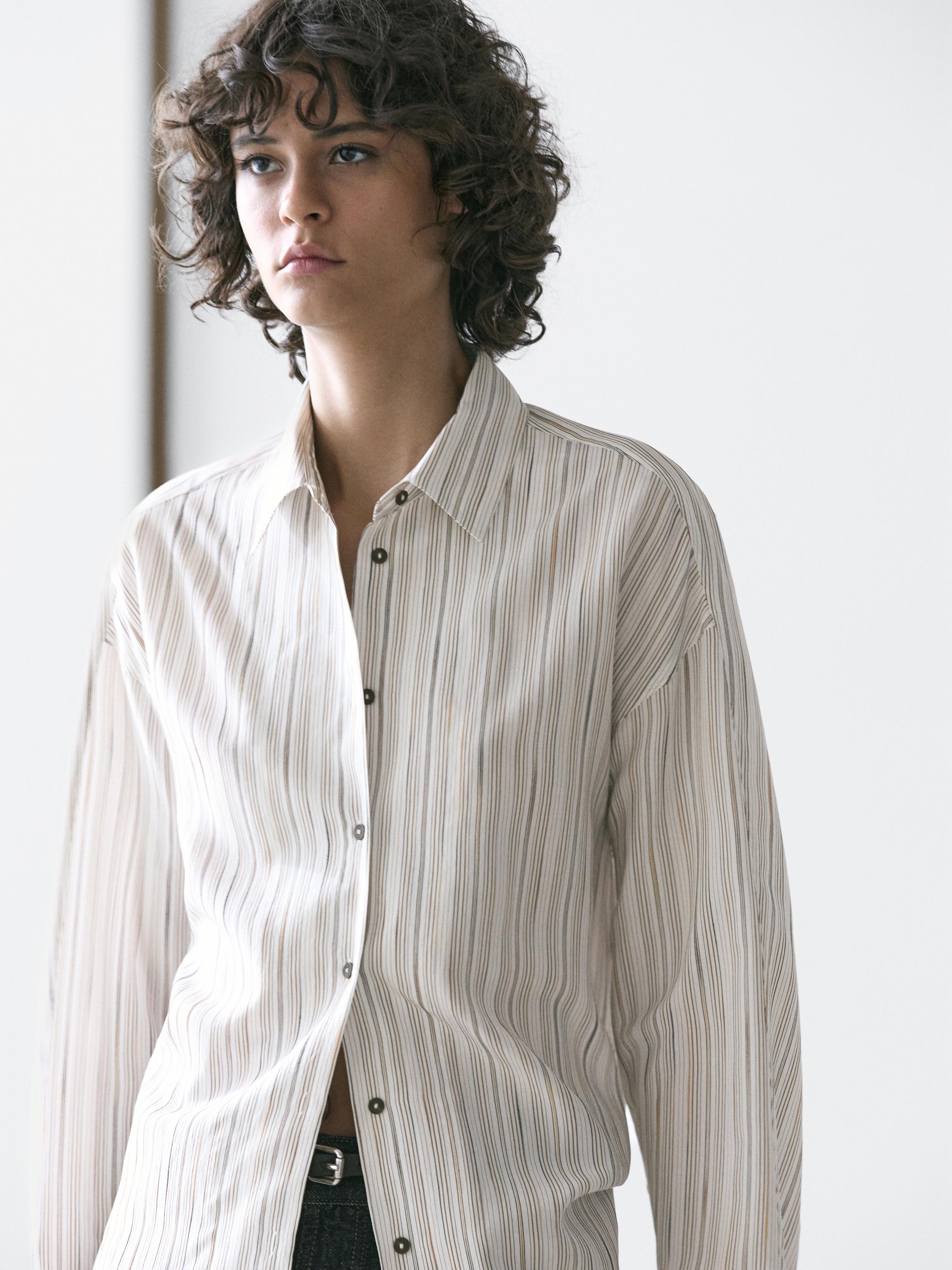 Plano medio de camisa blanca fluida con rayas verticales y botonadura frontal.