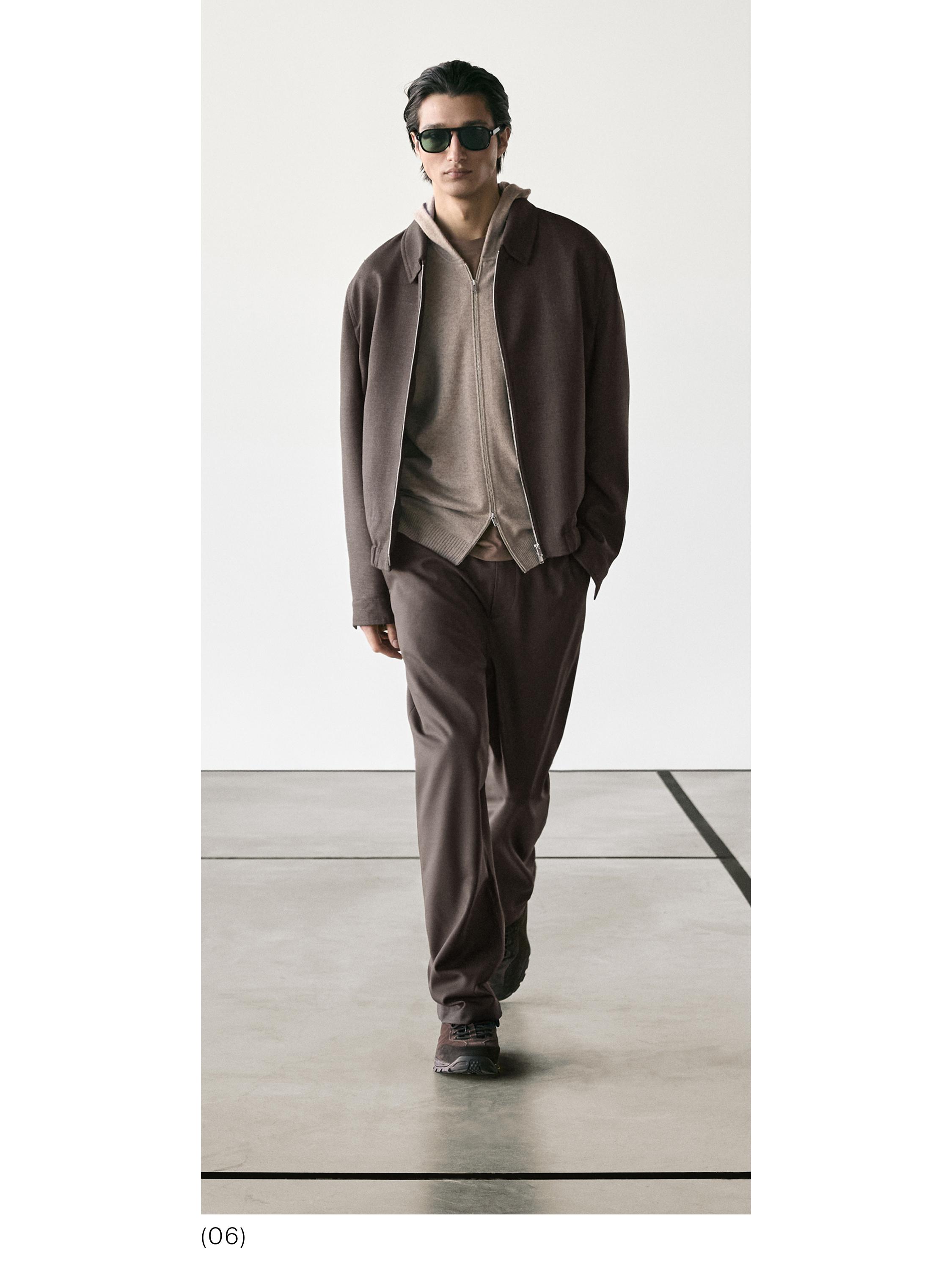 Conjunto de chaqueta marrón con cremallera, sudadera beige con capucha y pantalones marrones.