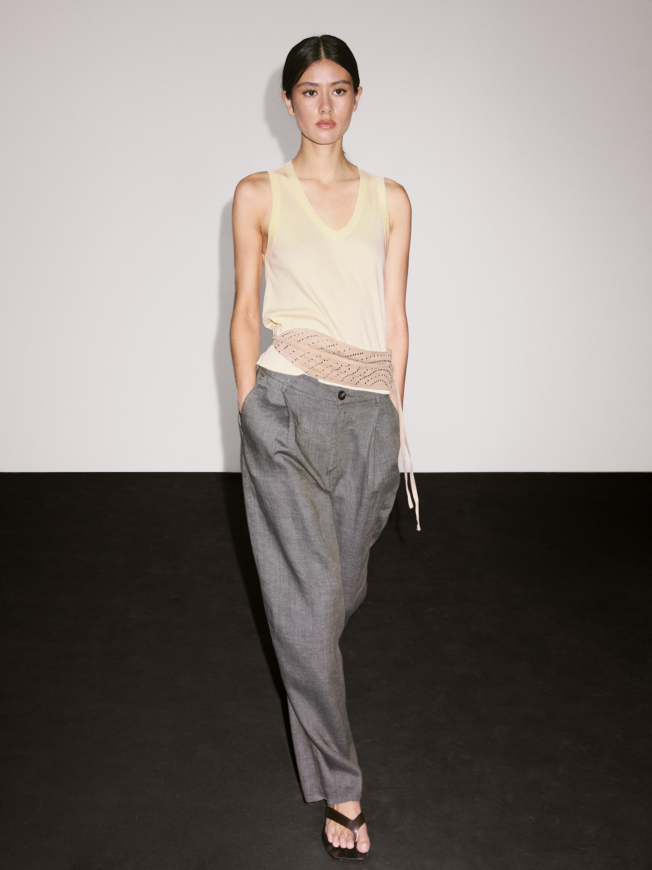 Ensemble composé d'un débardeur écru à col en V avec détail ajouré sur le côté, d'un pantalon gris à coupe ample et de sandales noires.