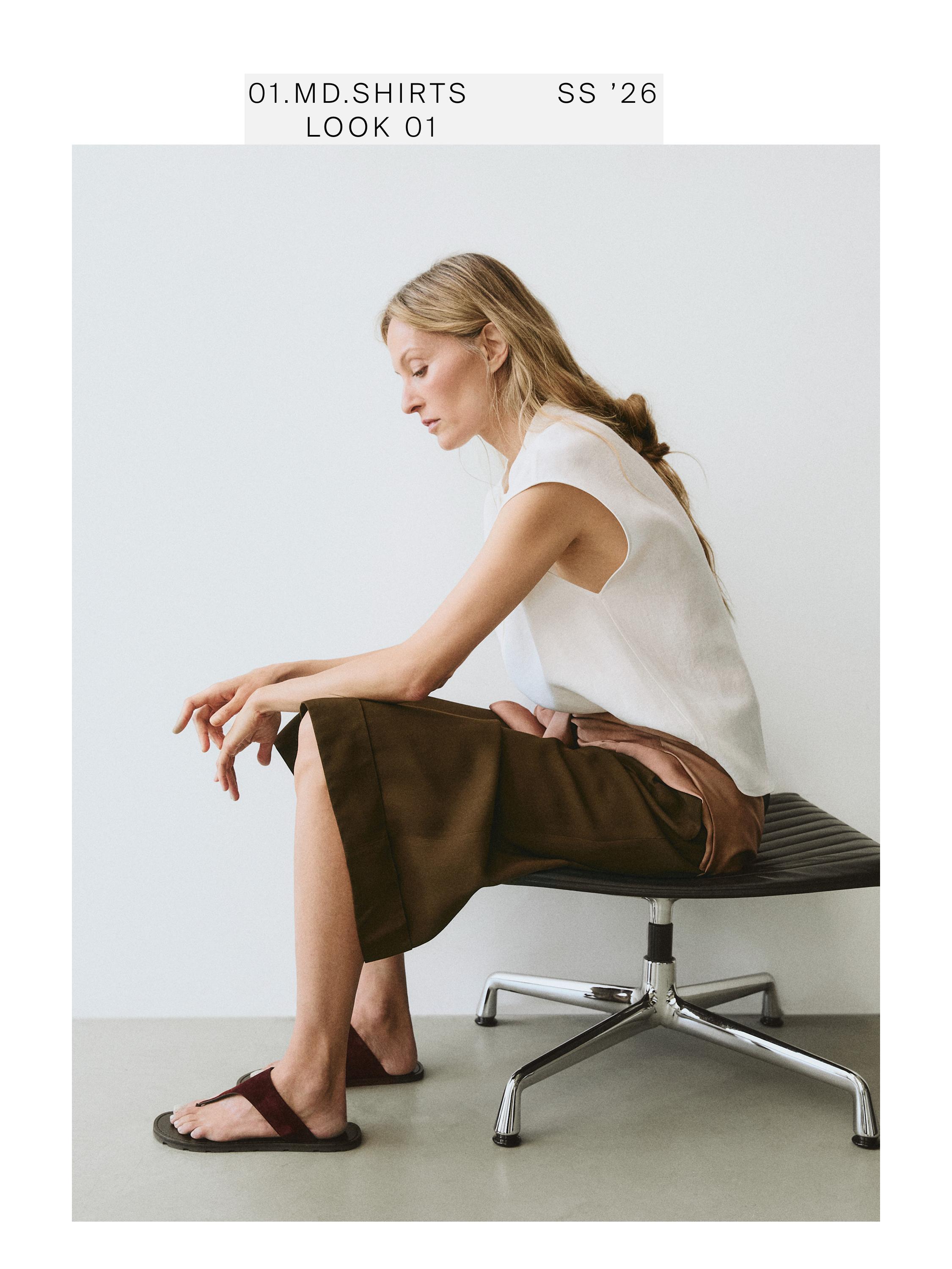 Medium shot of a white sleeveless shirt and a brown skirt. Visible text: "01.MD.SHIRTS SS '26 LOOK 01".