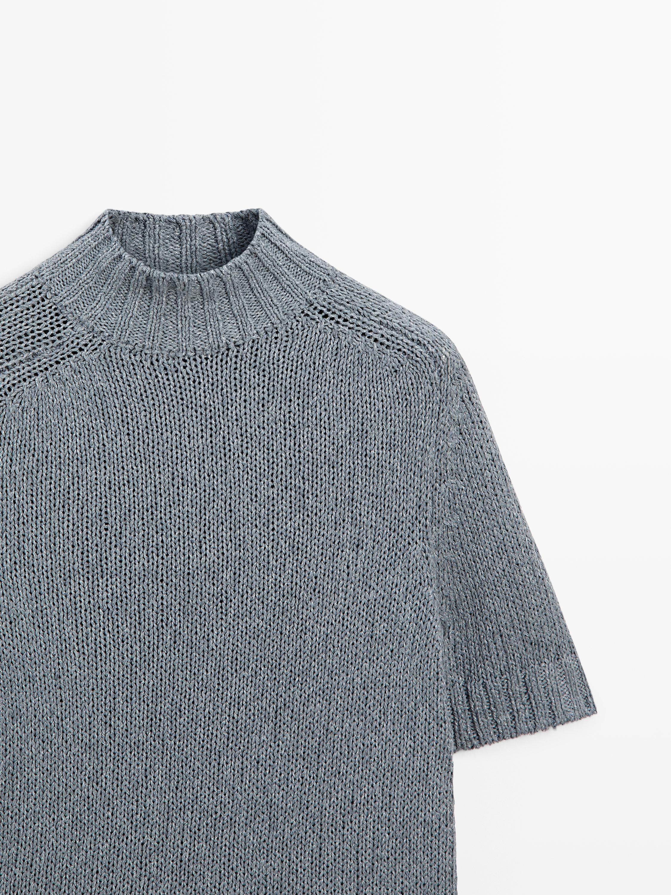"Detalle de suéter azul gris de punto con cuello tortuga y manga corta."