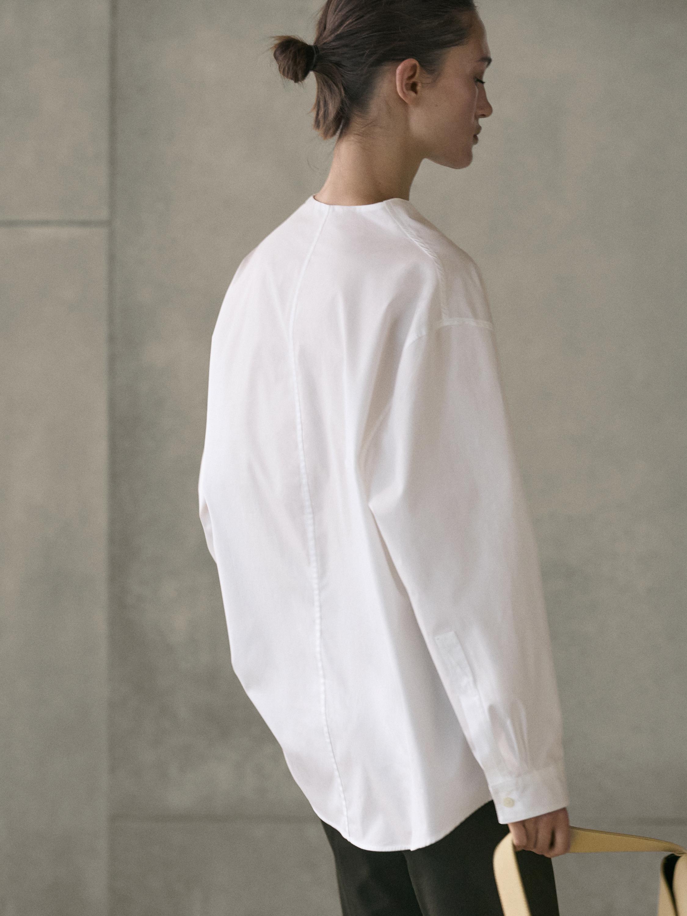 طقم قميص أبيض بأكمام طويلة مع درزة خلفية مركزية وبنطلون داكن.