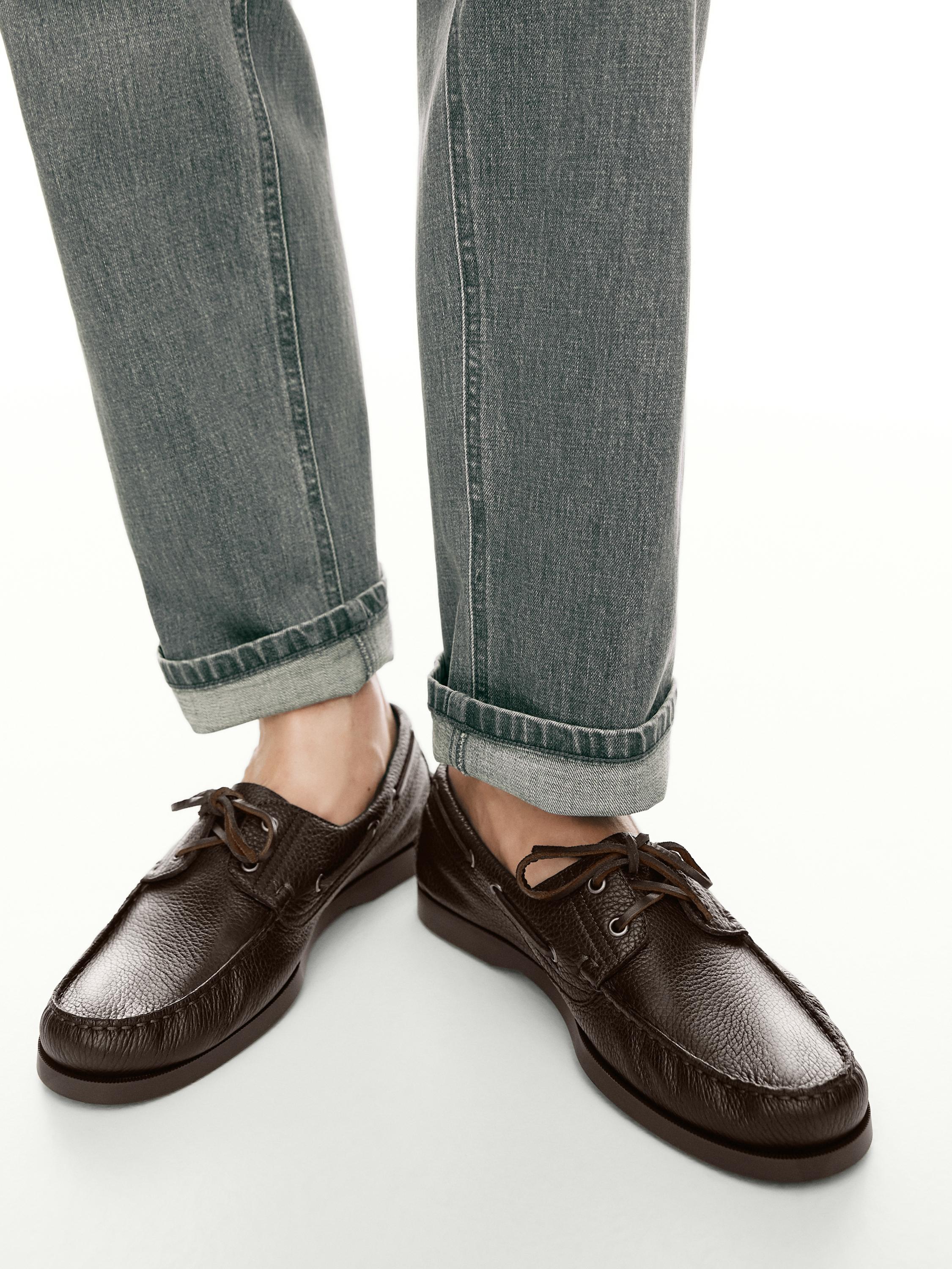 Bağcıklı kahverengi tekne ayakkabıları ve paçaları katlanmış gri kot pantolon kombinasyonu.