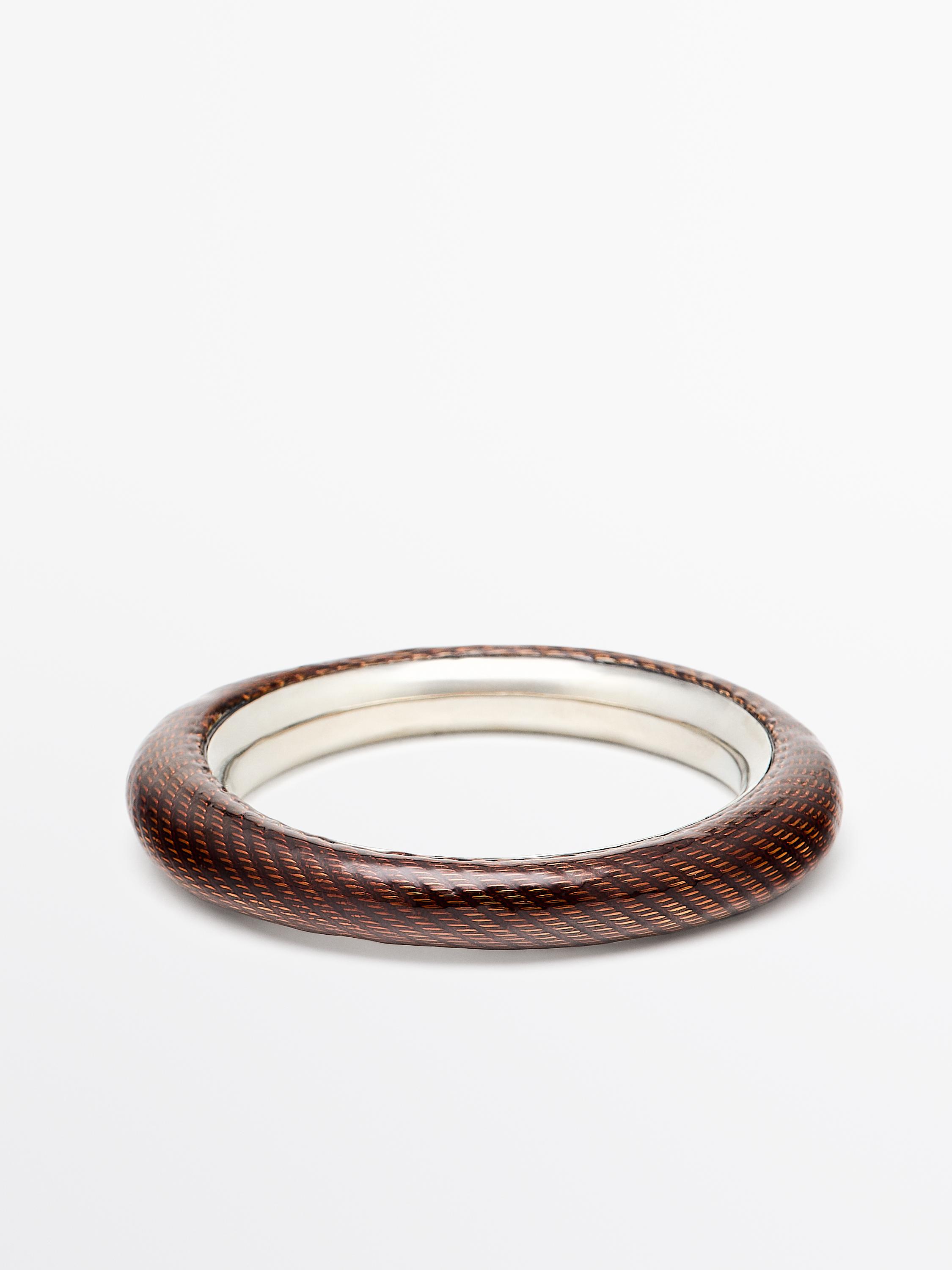 Άκαμπτο βραχιόλι σε ασημί χρώμα με εξωτερικό καφέ ανάγλυφο σχέδιο.