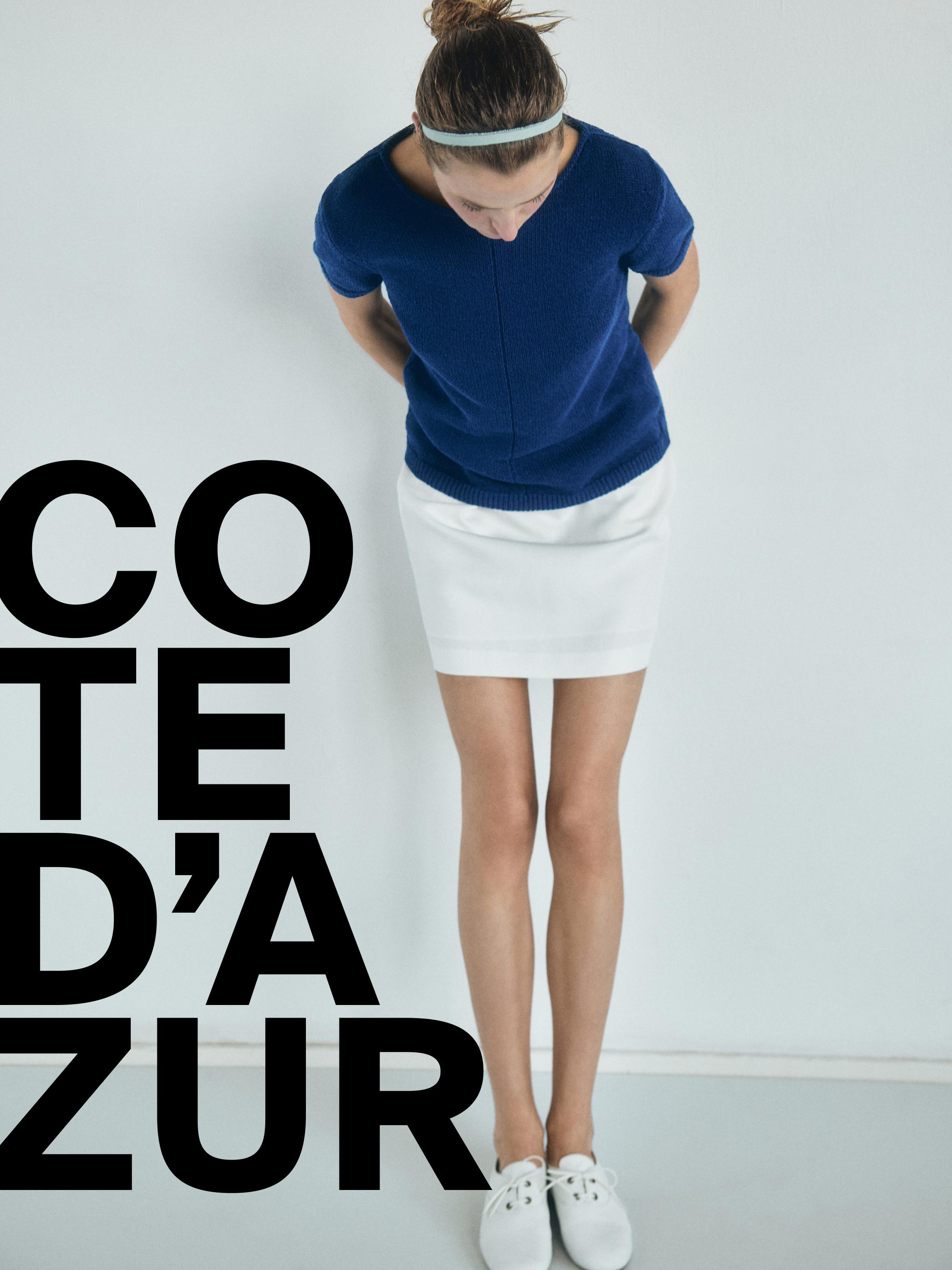 Σετ μπλε μπλούζας και κοντής λευκής φούστας. Ορατό κείμενο: "COTE D'AZUR". Λευκά παπούτσια.