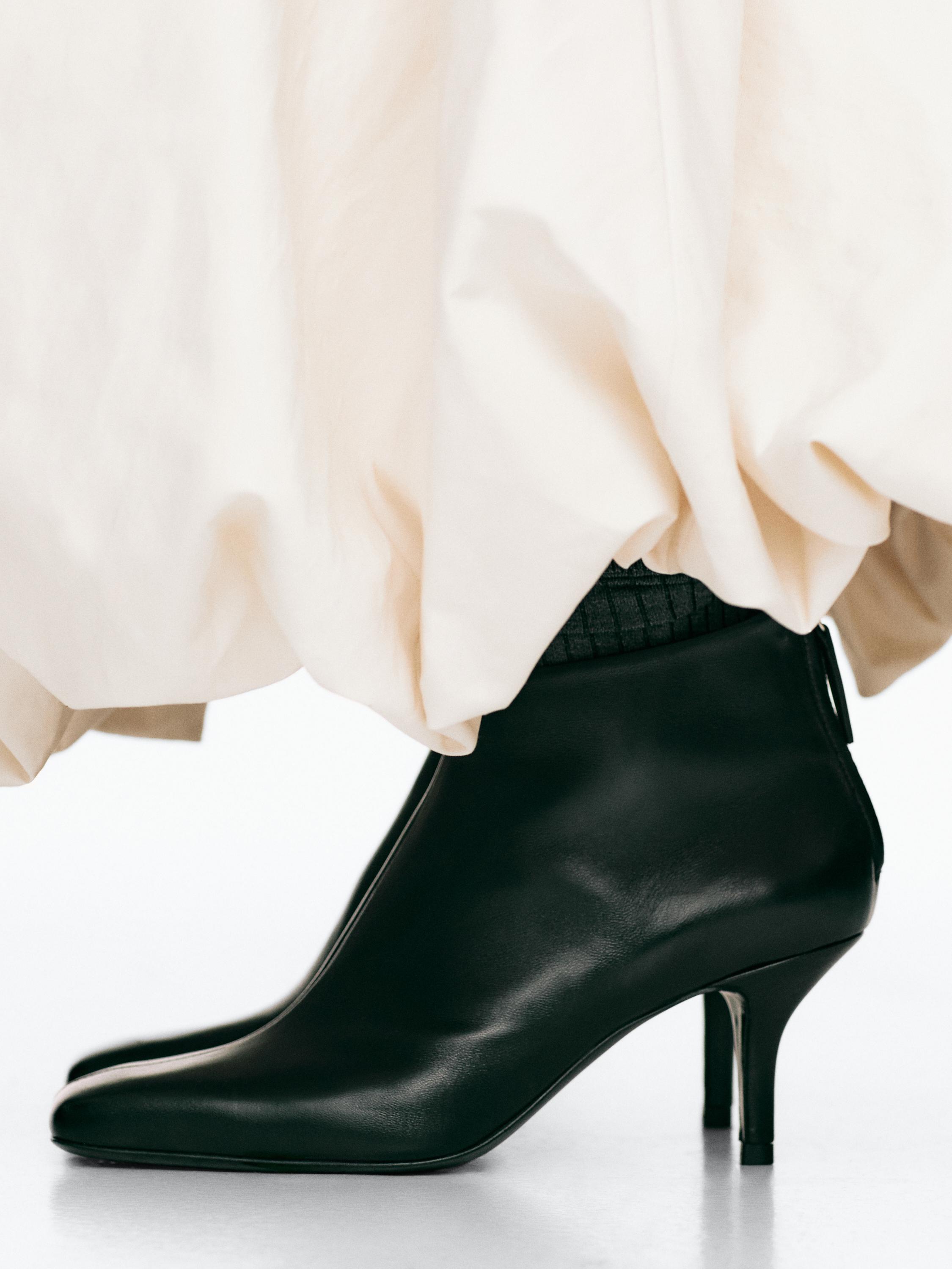 Détail de bottines noires à talon haut avec fermeture éclair arrière.