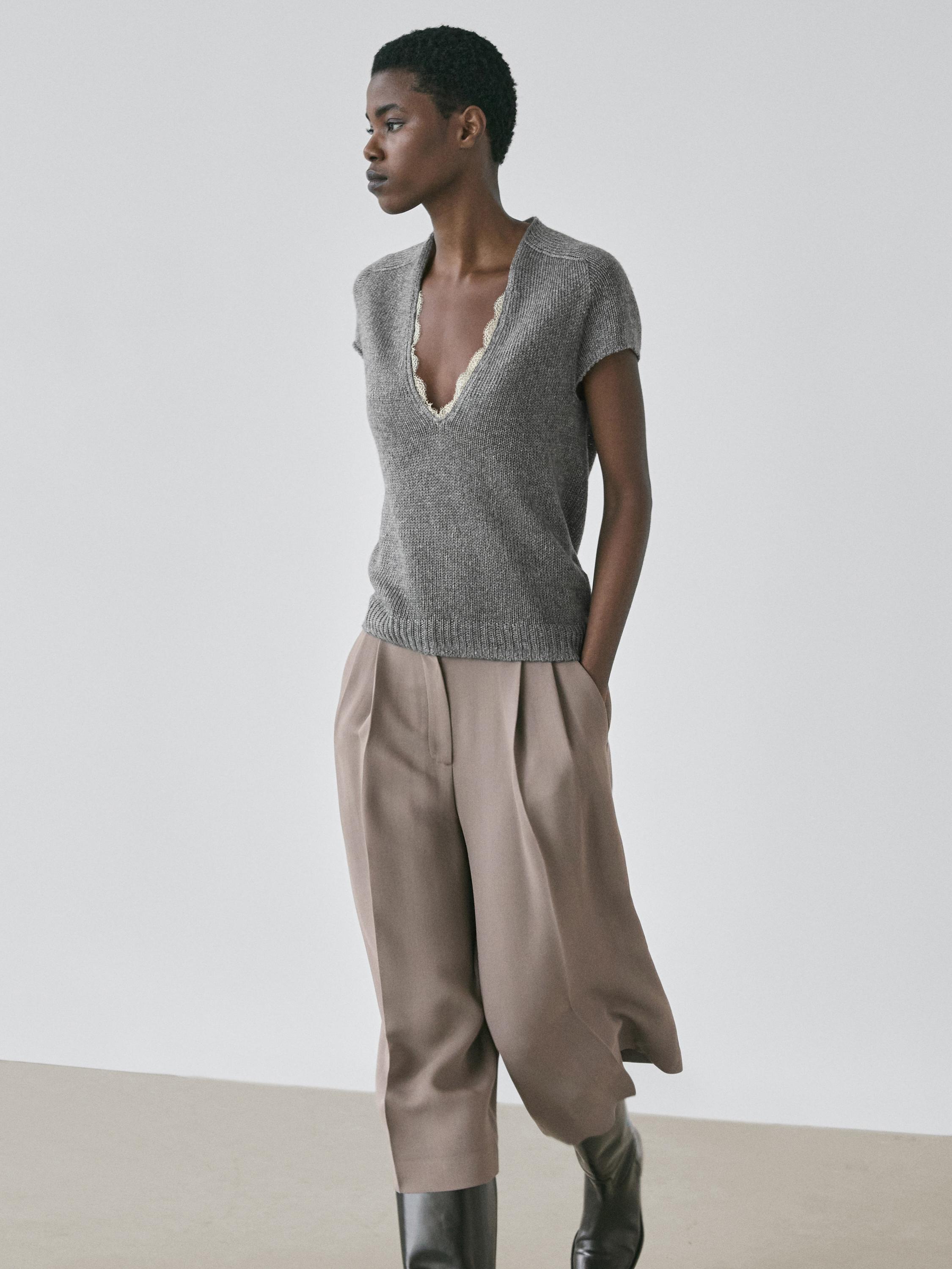 طقم سويتر رمادي متوسط برقبة على شكل V ودانتيل، بنطلون بيج واسع، وبوت أسود.