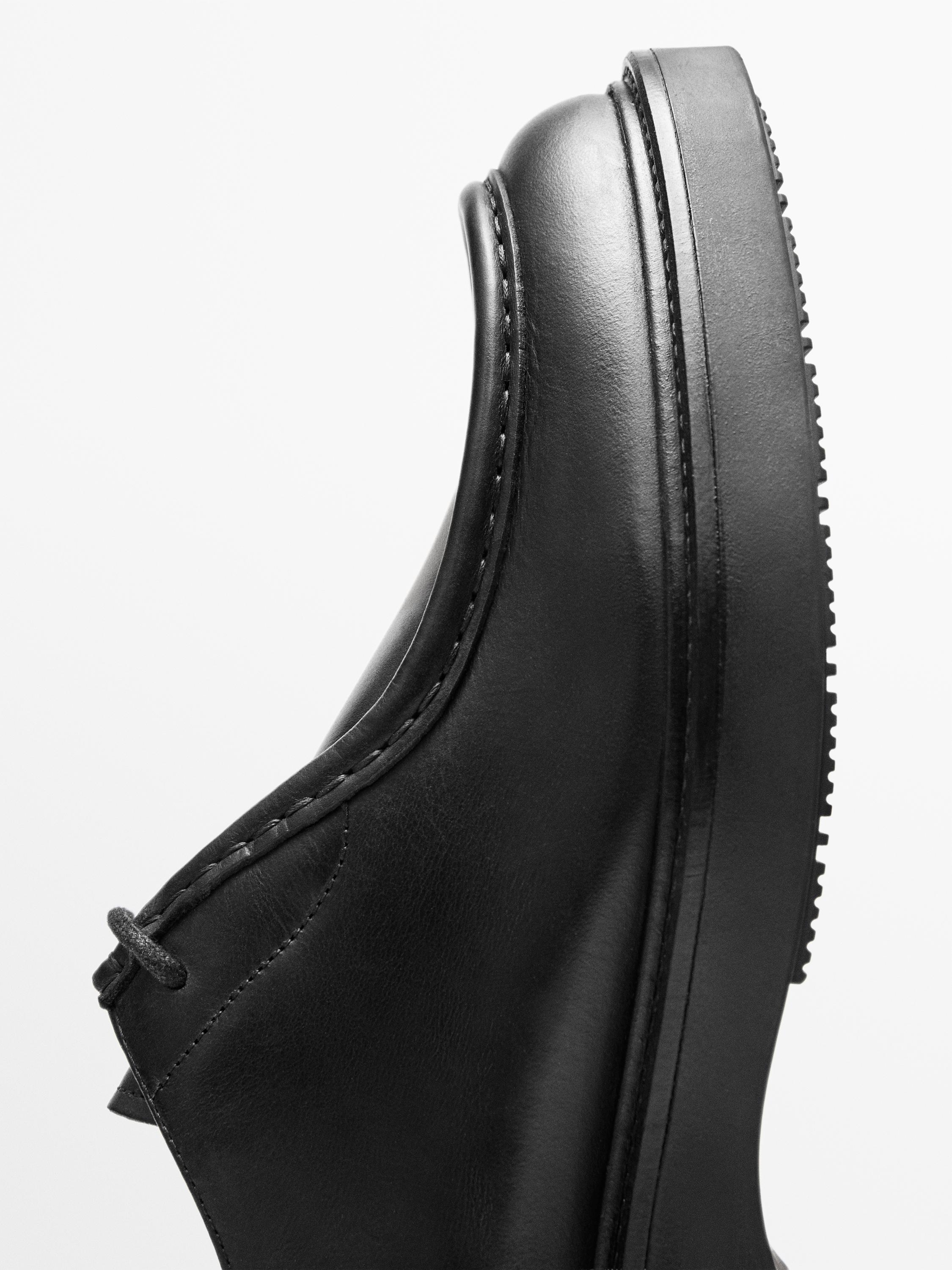 Détail d'une chaussure noire avec surpiqûres visibles et semelle épaisse.