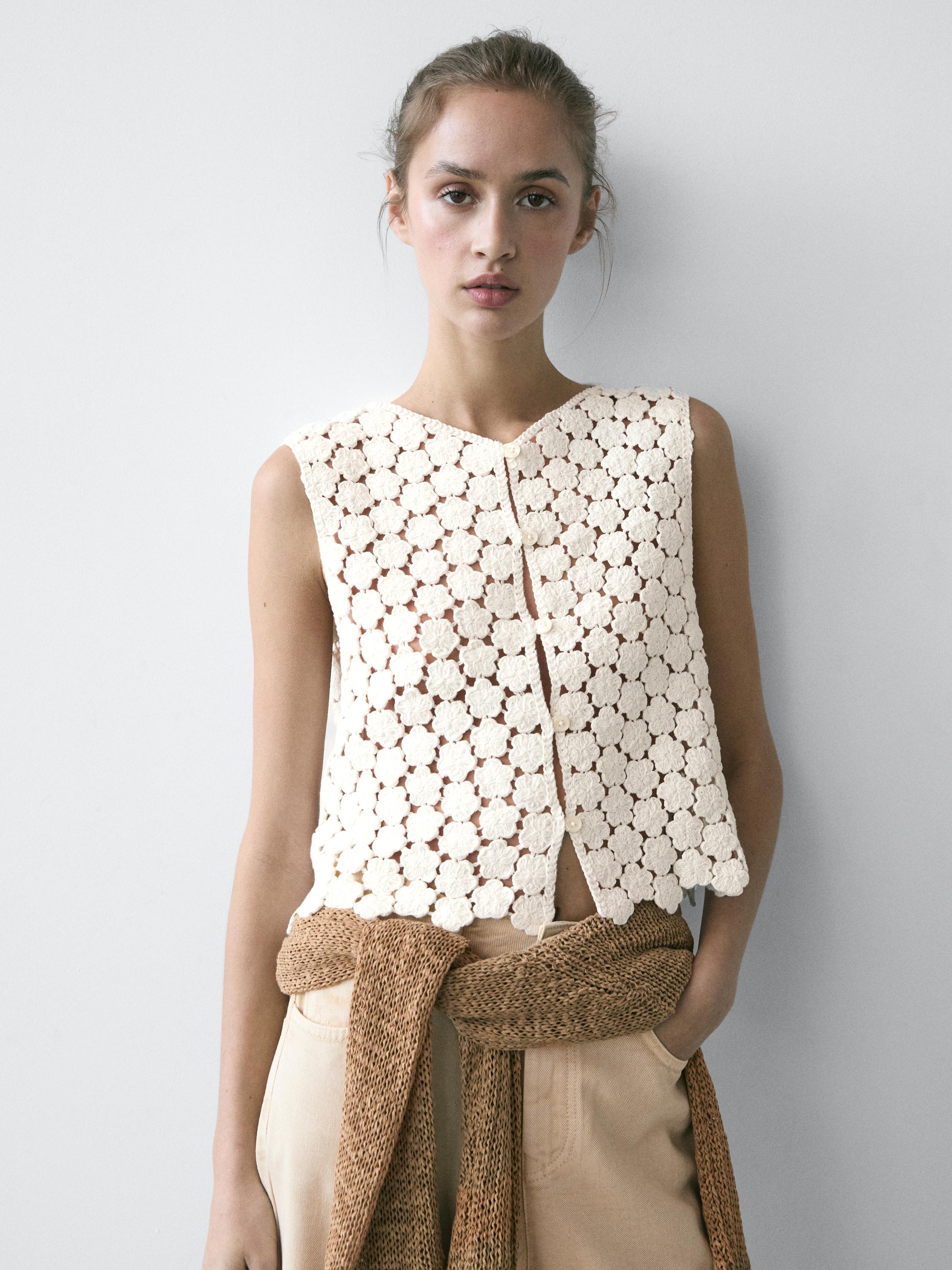 Półzbliżenie na surową kamizelkę szydełkową z detalami kwiatowymi i zapięciem na guziki z przodu.