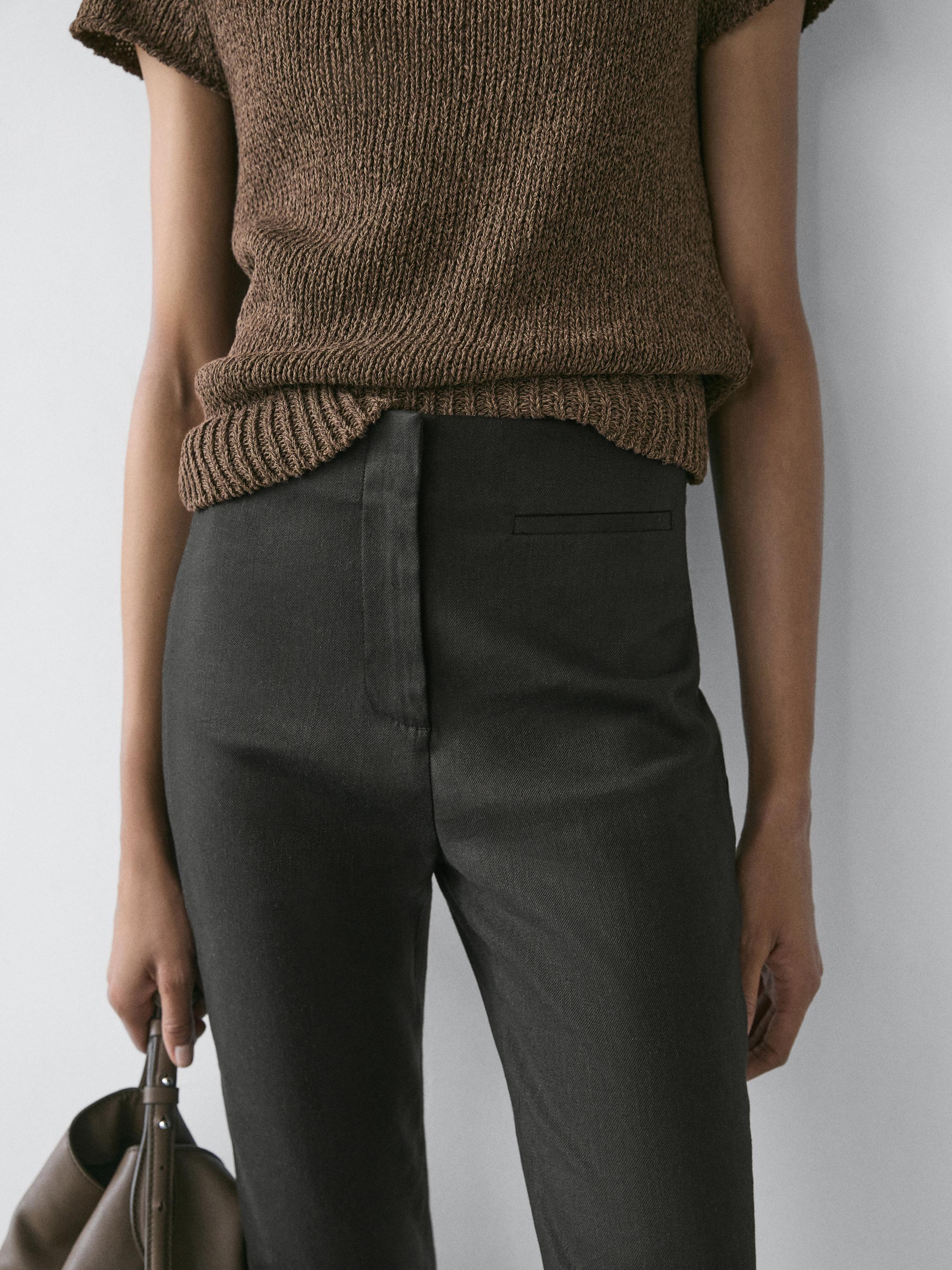 Plano médio de calças capri pretas com bolsos frontais, combinadas com camisola castanha de malha.