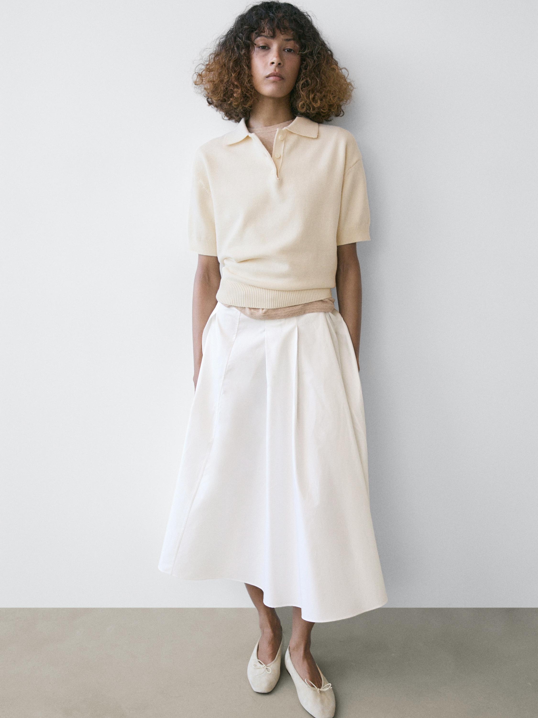 Conjunto de jersey polo blanco roto de manga corta y falda larga blanca con pliegues.