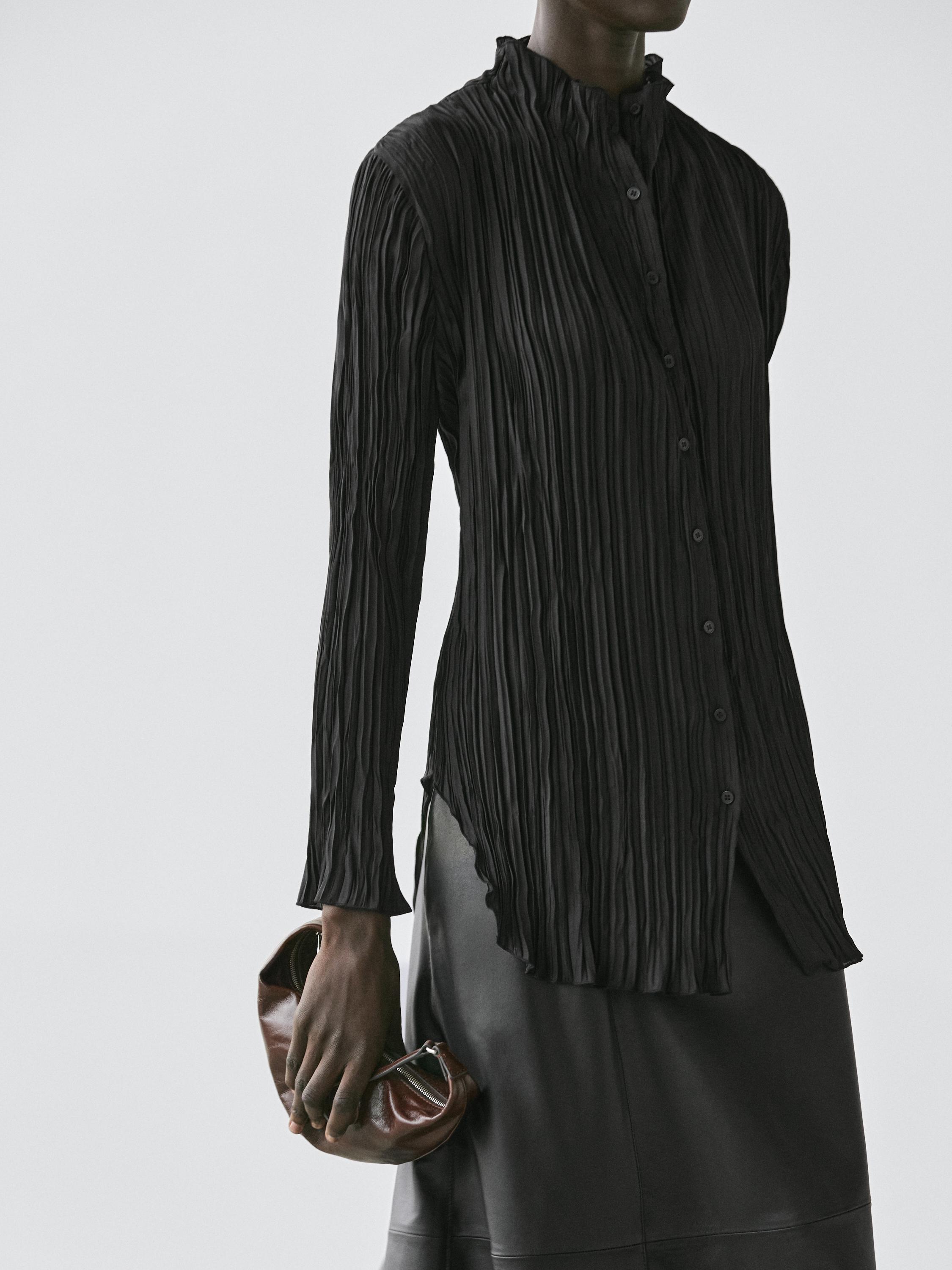 Средний план струящейся черной рубашки с плиссированными деталями и передней планкой на пуговицах.