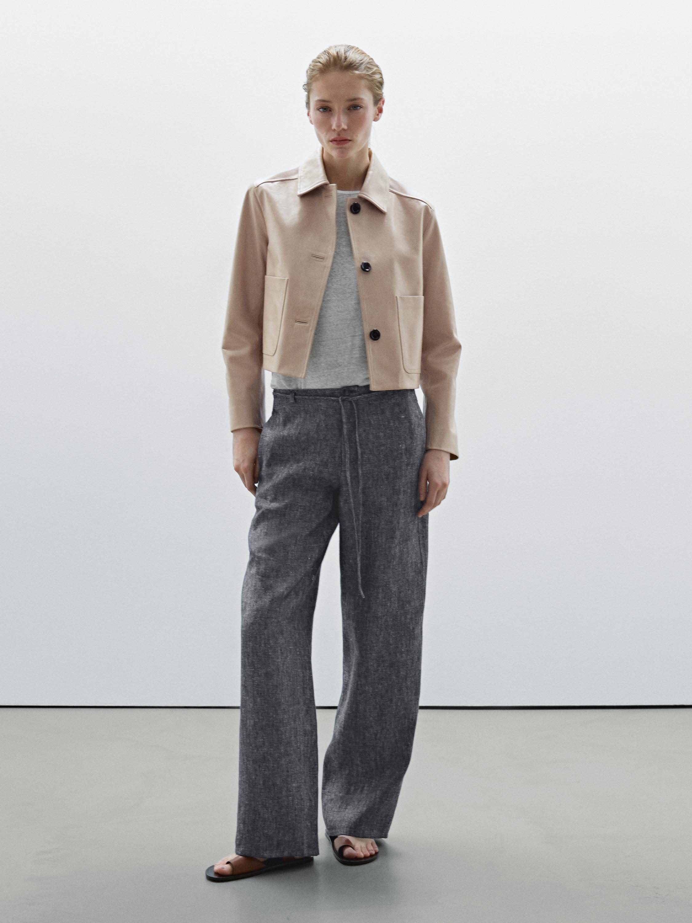 Ensemble veste beige avec poches avant et boutons noirs, pantalon gris à jambes larges et sandales noires.