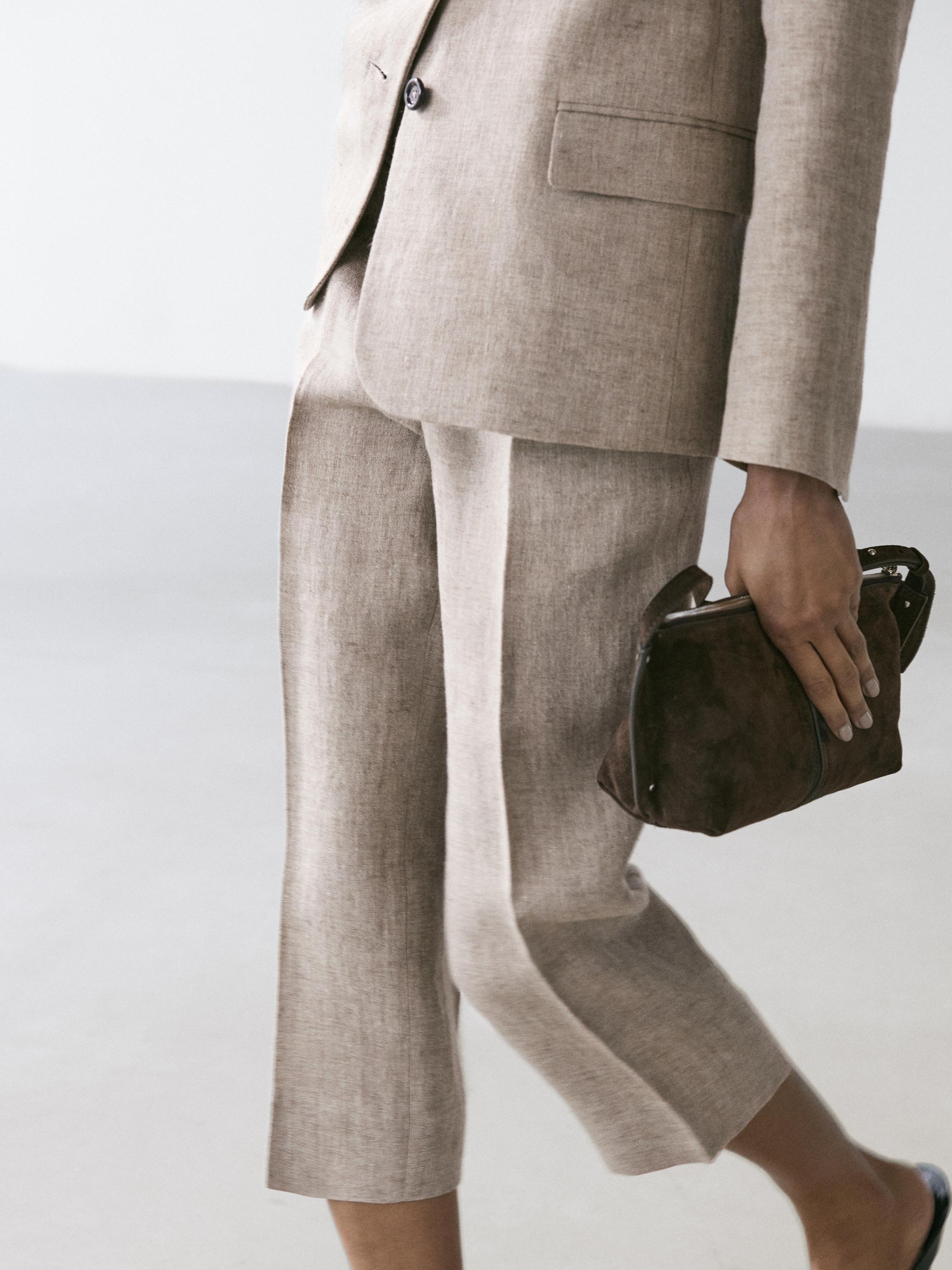 Plano médio de calças bege com bolsos laterais e blazer a combinar.