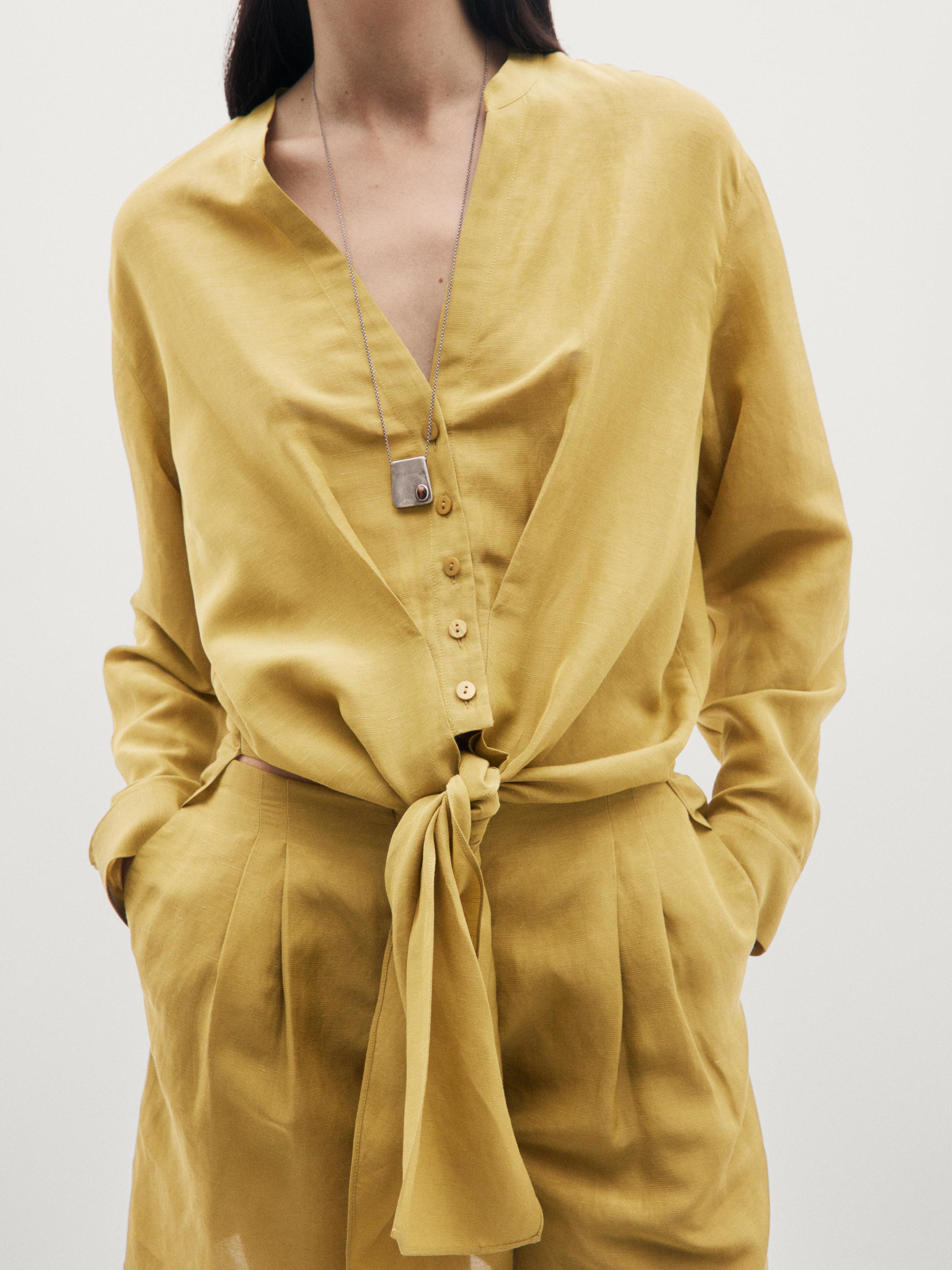 Plano medio de camisa color pistache con nudo y botones, bolsillos laterales visibles.
