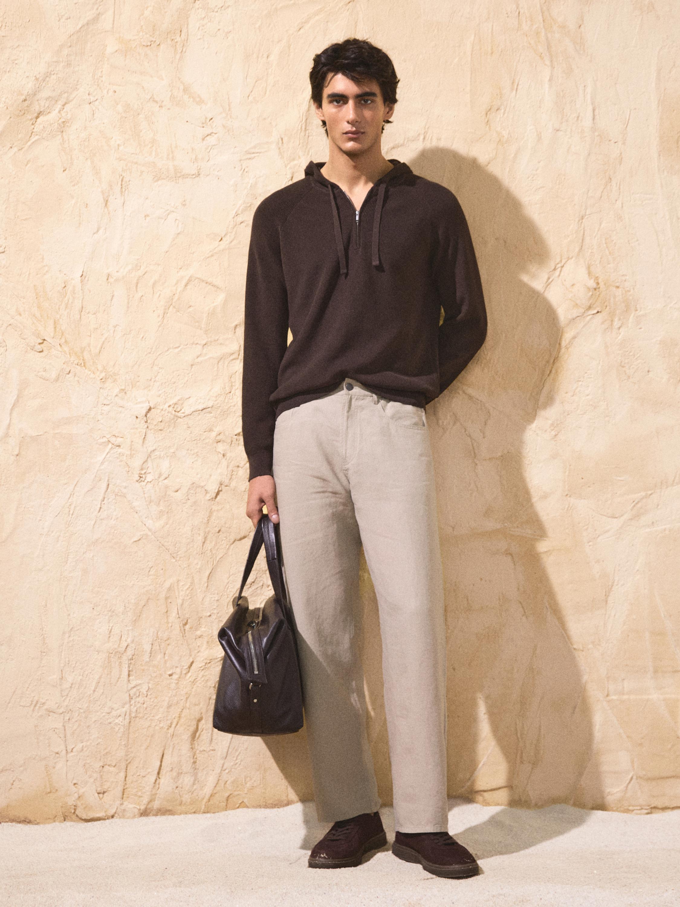 طقم هودي بني وبنطلون بيج مستقيم. ترتدي حقيبة داكنة وحذاء بني.