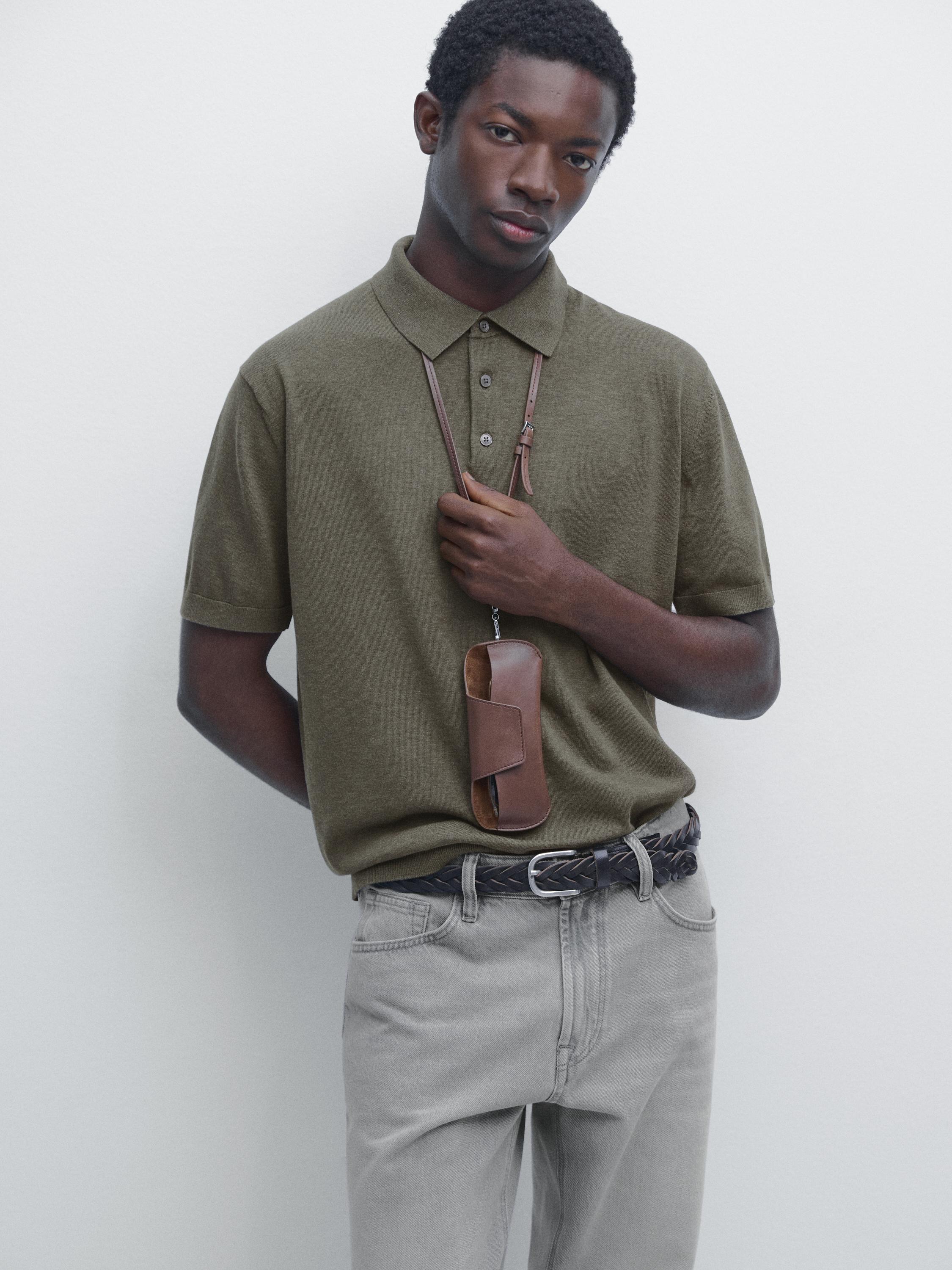 Medium shot of a green polo sweater with a classic collar and buttons, paired with gray pants and a braided belt.