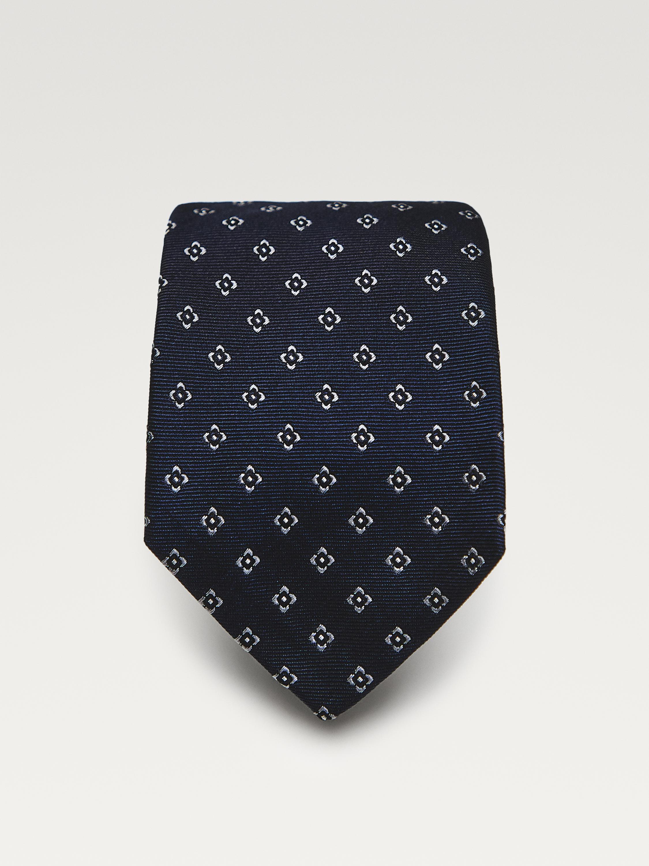 Front view of a navy blue tie with a pattern of small white geometric motifs.