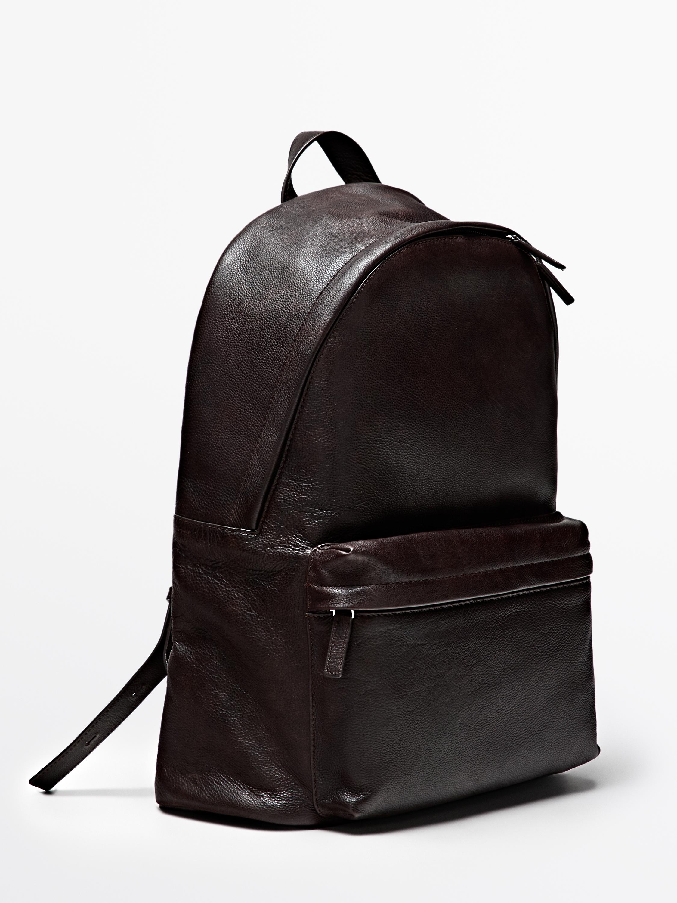 Side view of a brown backpack with a top zipper and a front zipper pocket. Top handle and adjustable straps visible.