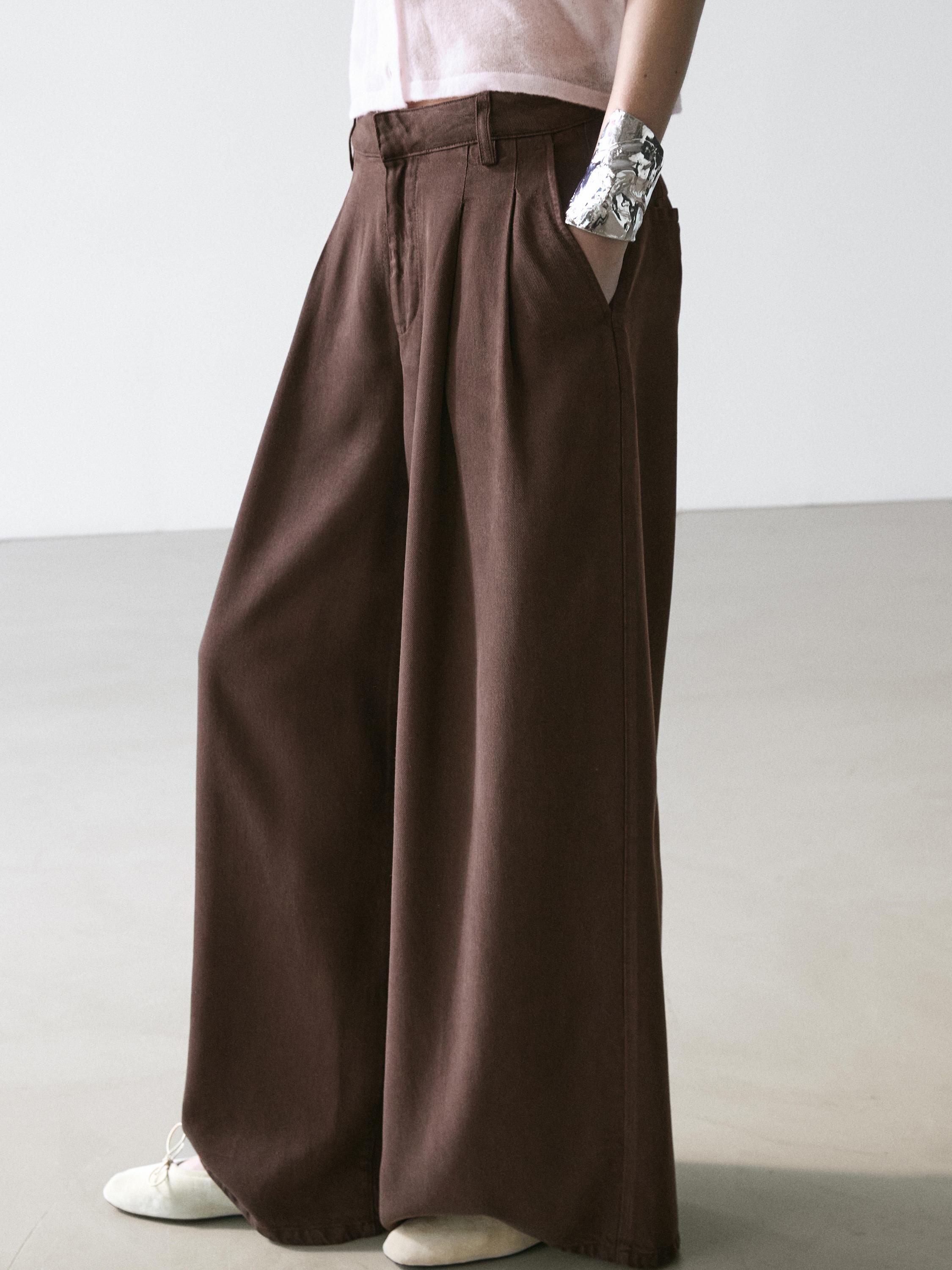 Plano medio de pantalón chocolate wide leg con pliegues y bolsillos laterales.
