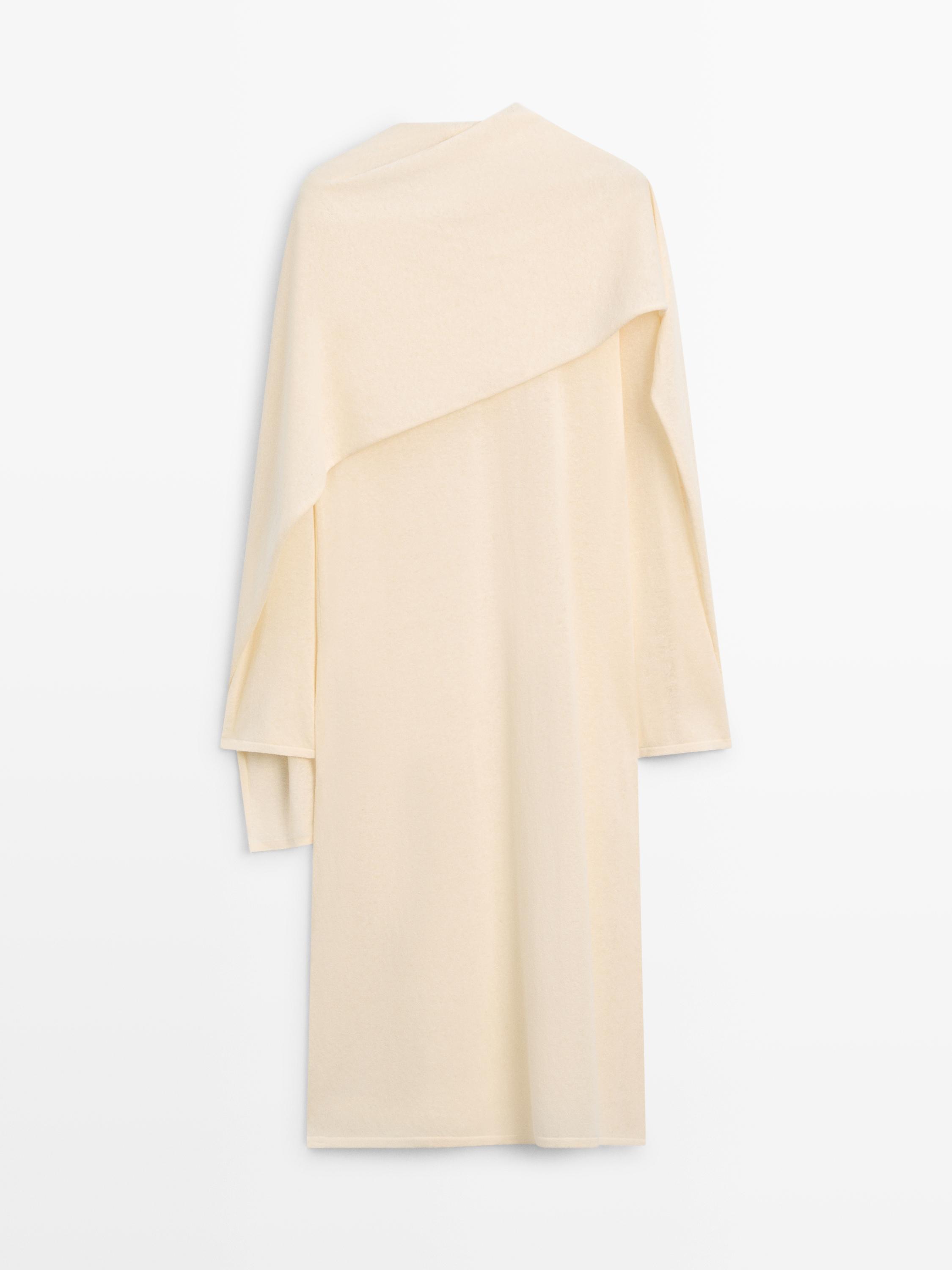 Asimetriadun diseinua eta mahuka luzeak dituen bainila koloreko soinekoaren atzealdeko ikuspegia.