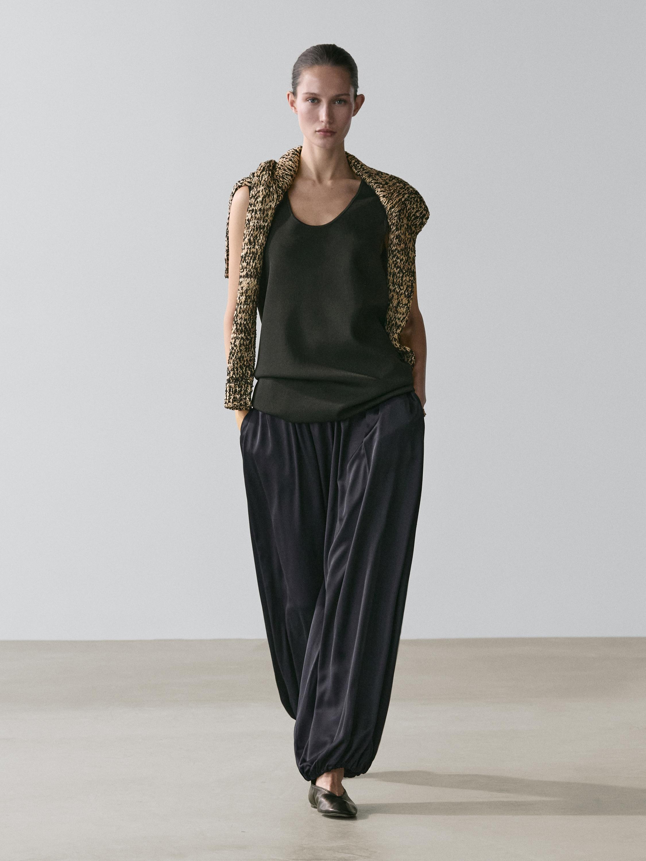 Dark blue balloon pants set and black sleeveless top, with a knitted jacket over the shoulders.