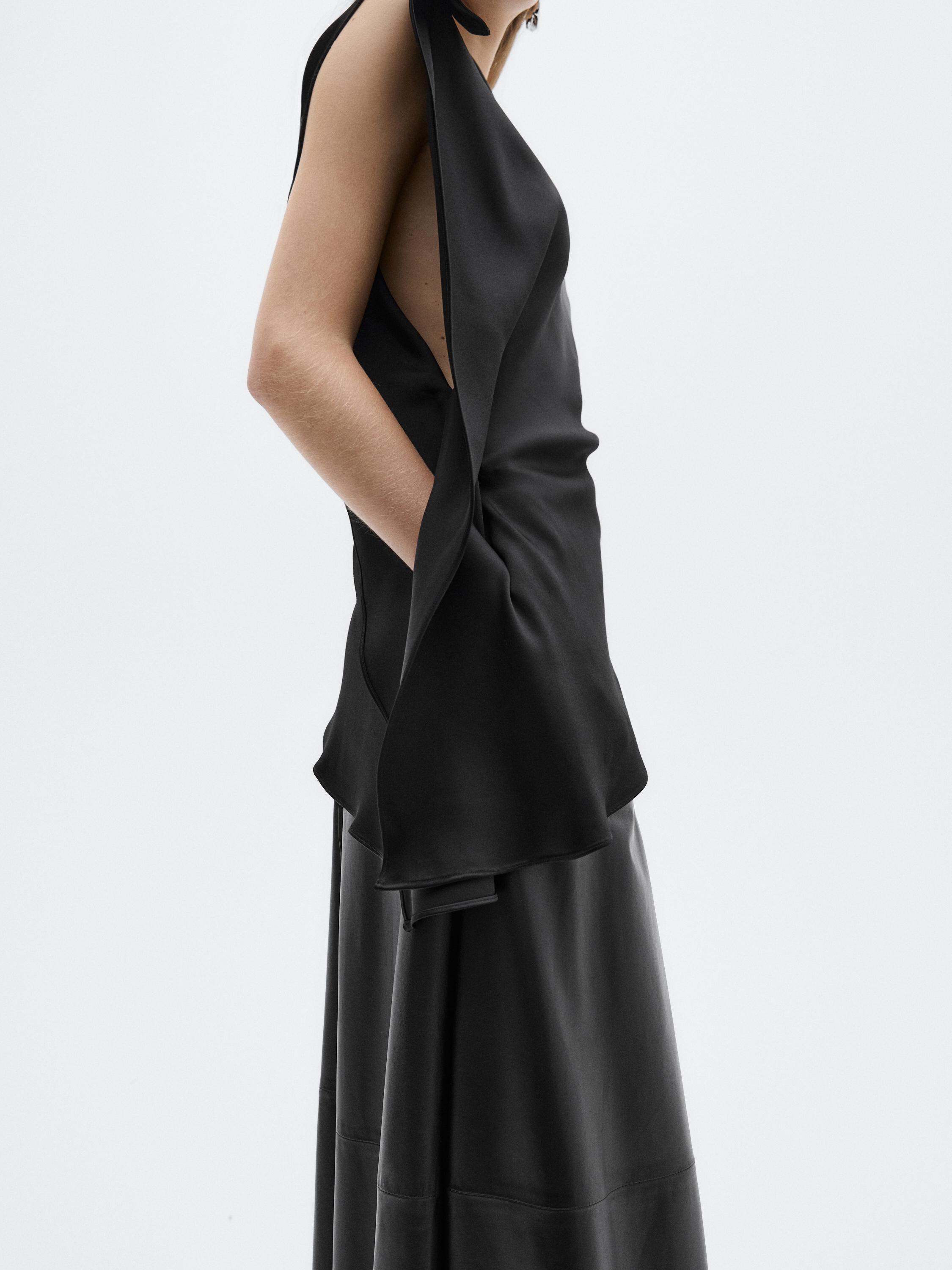 Halbaufnahme eines ärmellosen schwarzen Kleides mit Volant-Detail an der Seite und tiefem Ausschnitt.