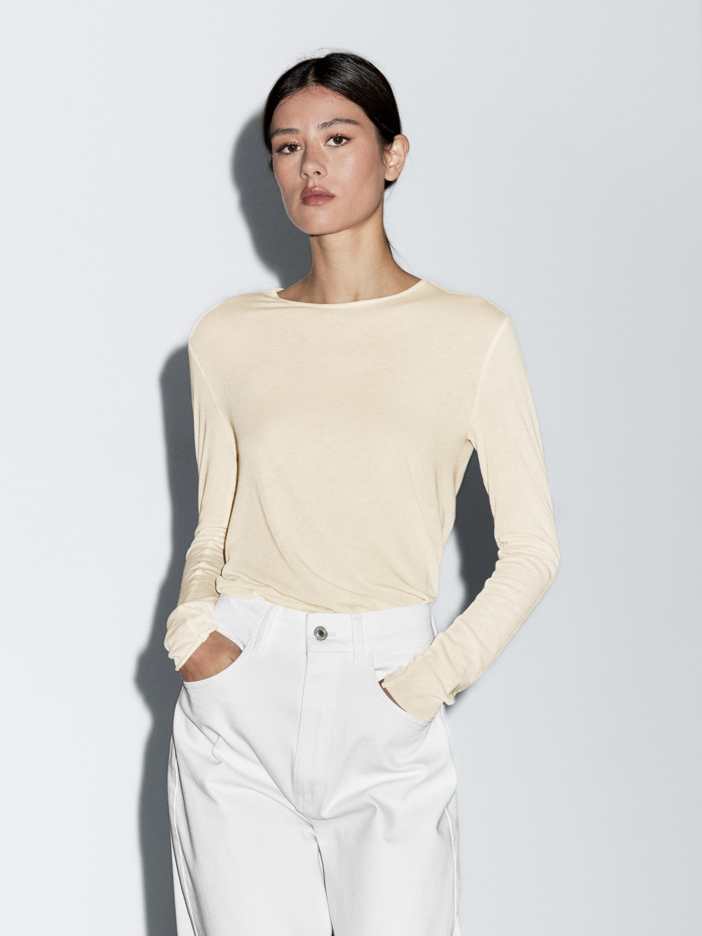 Комплет од беж маица со долги ракави и бели панталони со странични џебови.