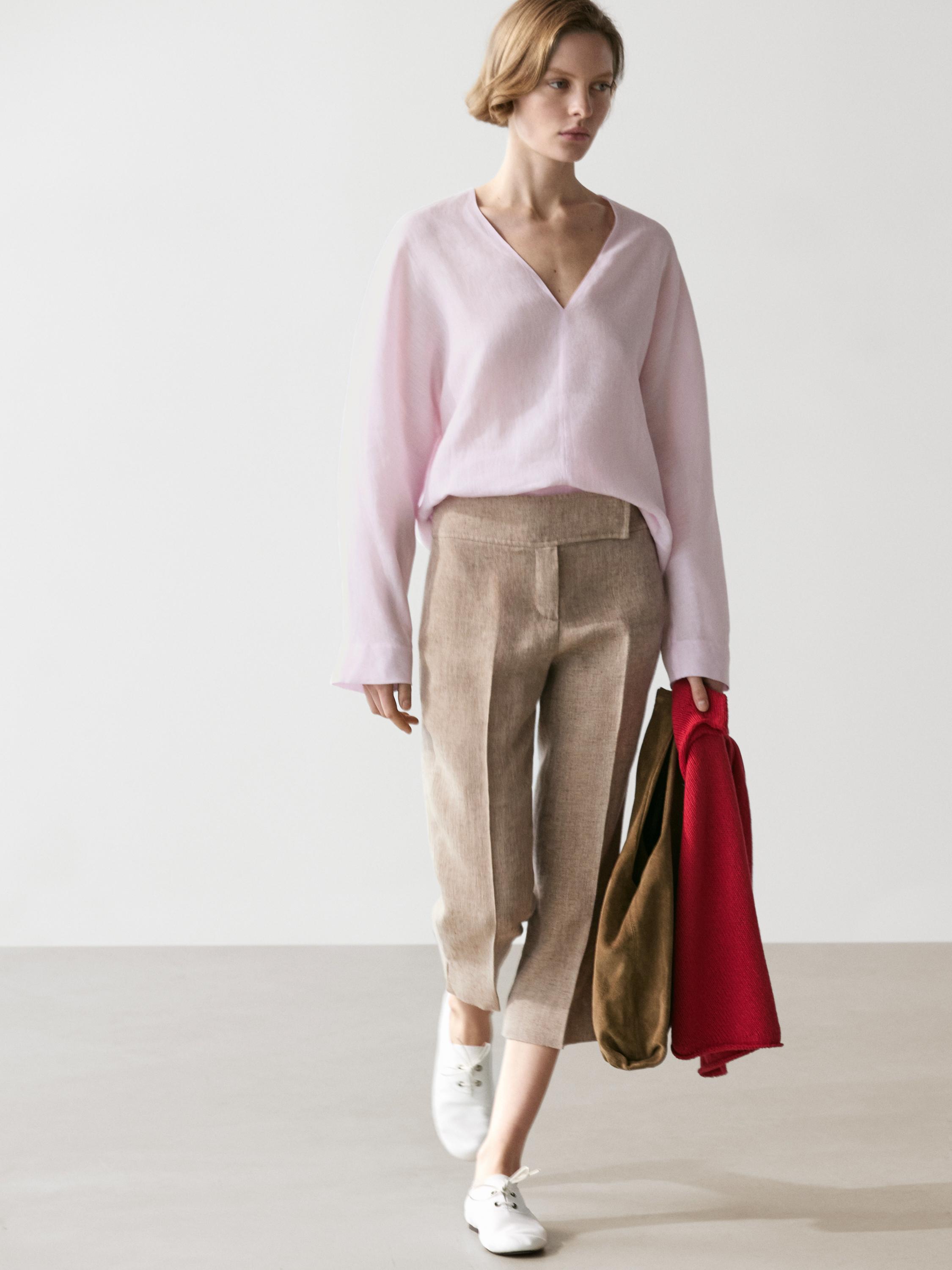 Σετ από ροζ μπλούζα με V λαιμόκοψη και μπεζ παντελόνι με μπροστινές τσέπες, λευκά παπούτσια και κόκκινο σακάκι στο χέρι.