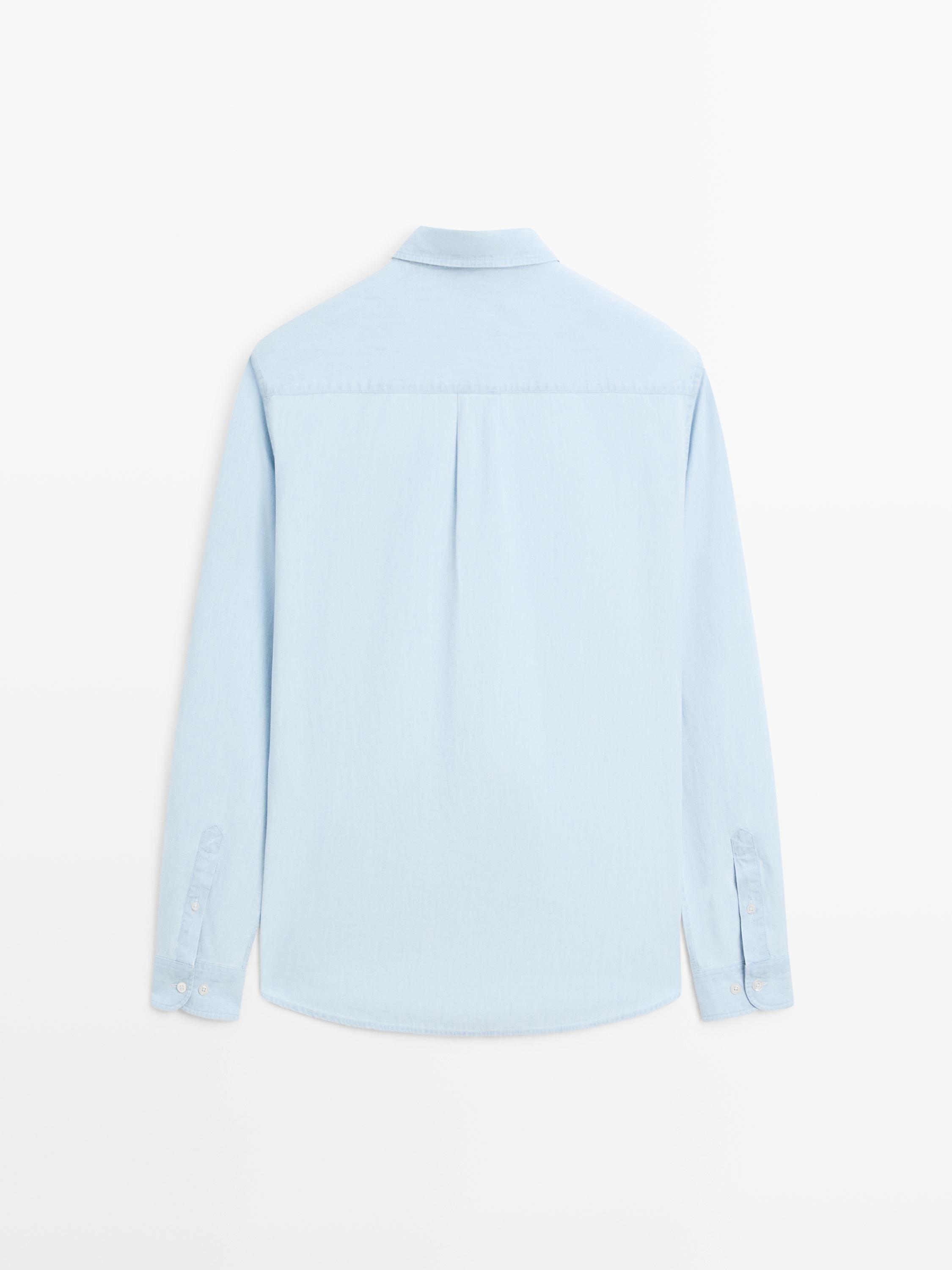มุมมองด้านหลังของเสื้อเชิ้ตแขนยาวสีฟ้าอ่อน มีข้อมือติดกระดุม และจีบกลางด้านหลัง