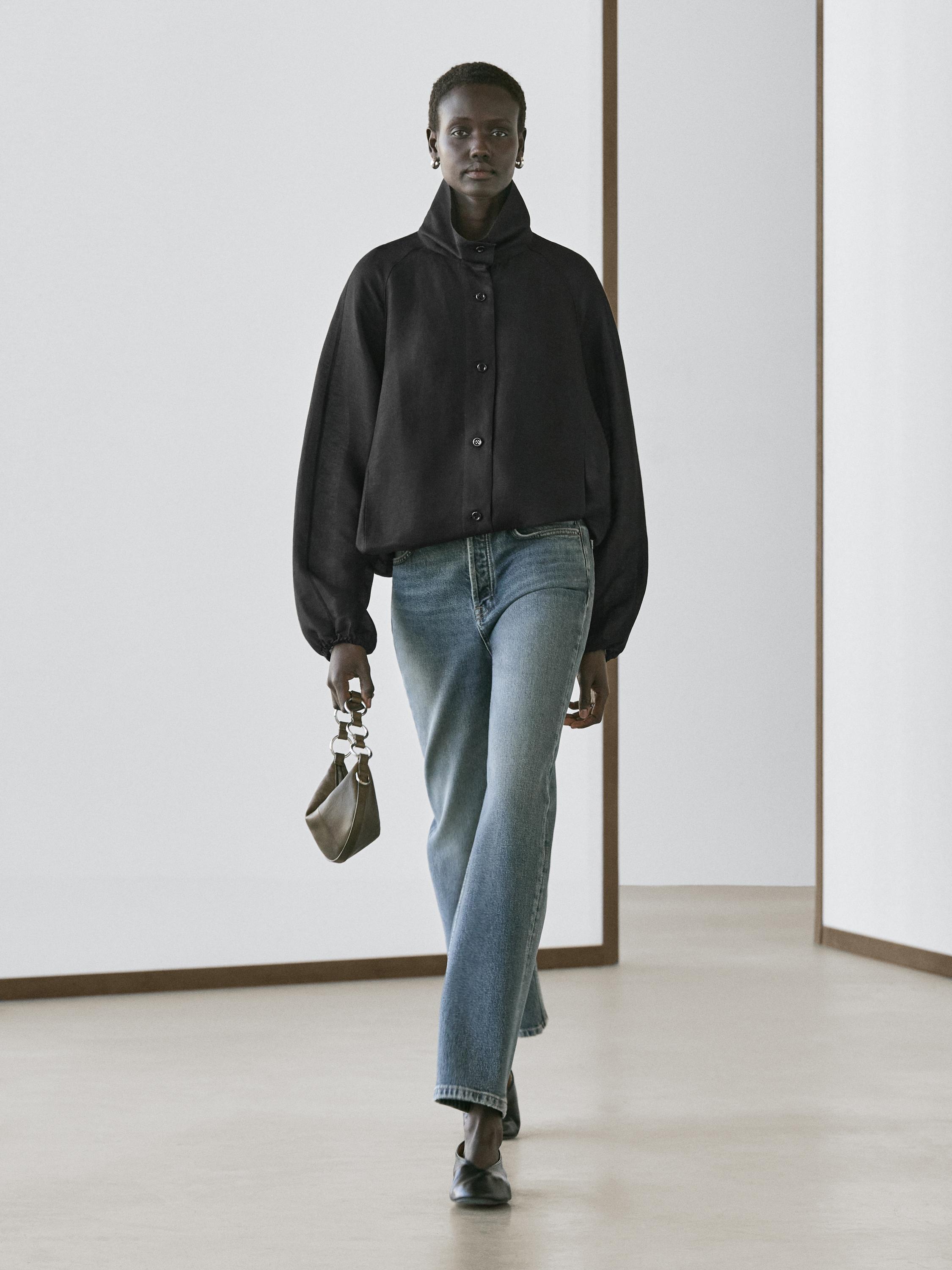 Schwarze Bomberjacke mit Knöpfen und gerade geschnittene blaue Jeans.