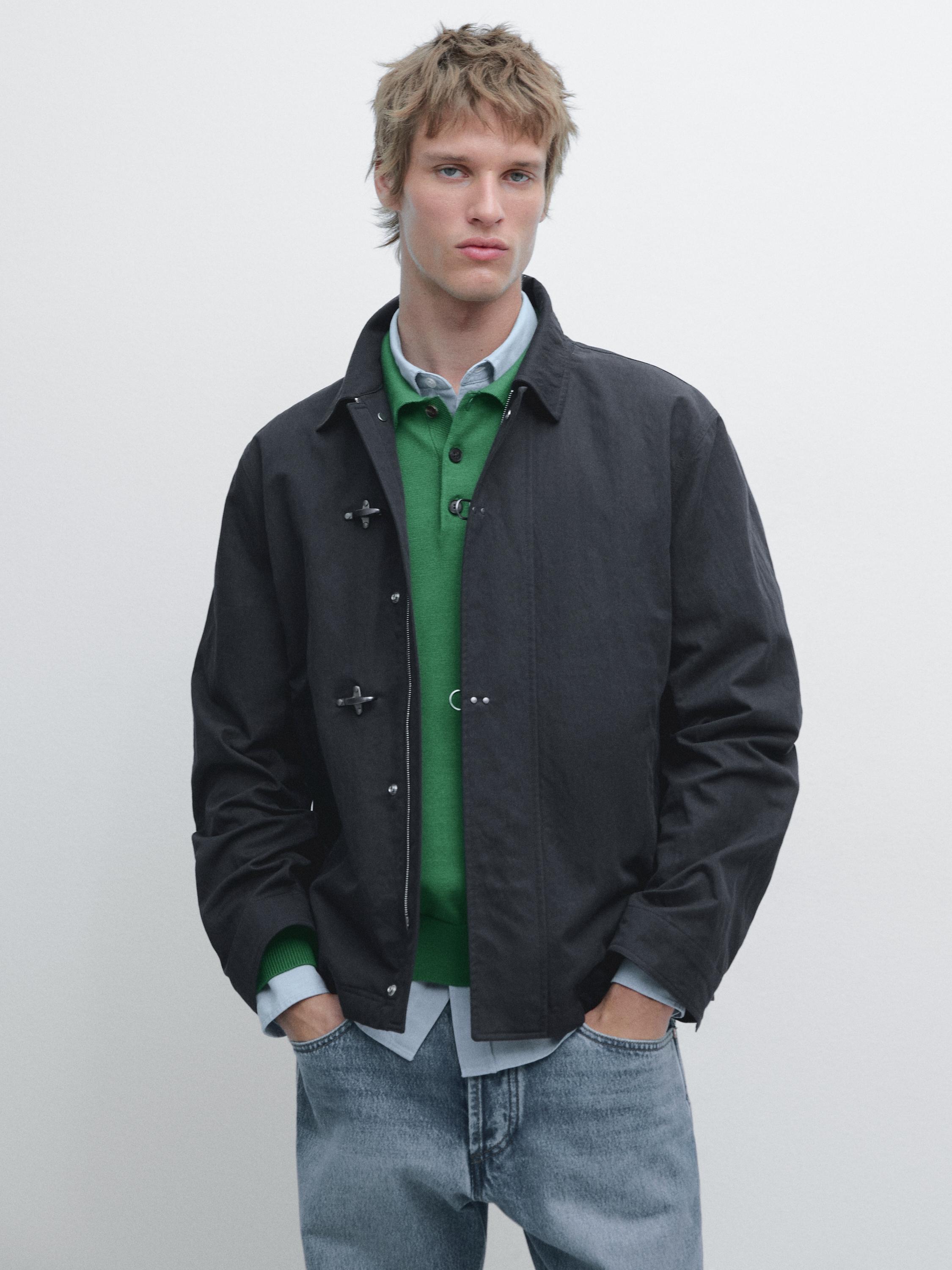 Navy blue jacket set with frogging, green sweater, light blue shirt, and blue jeans.