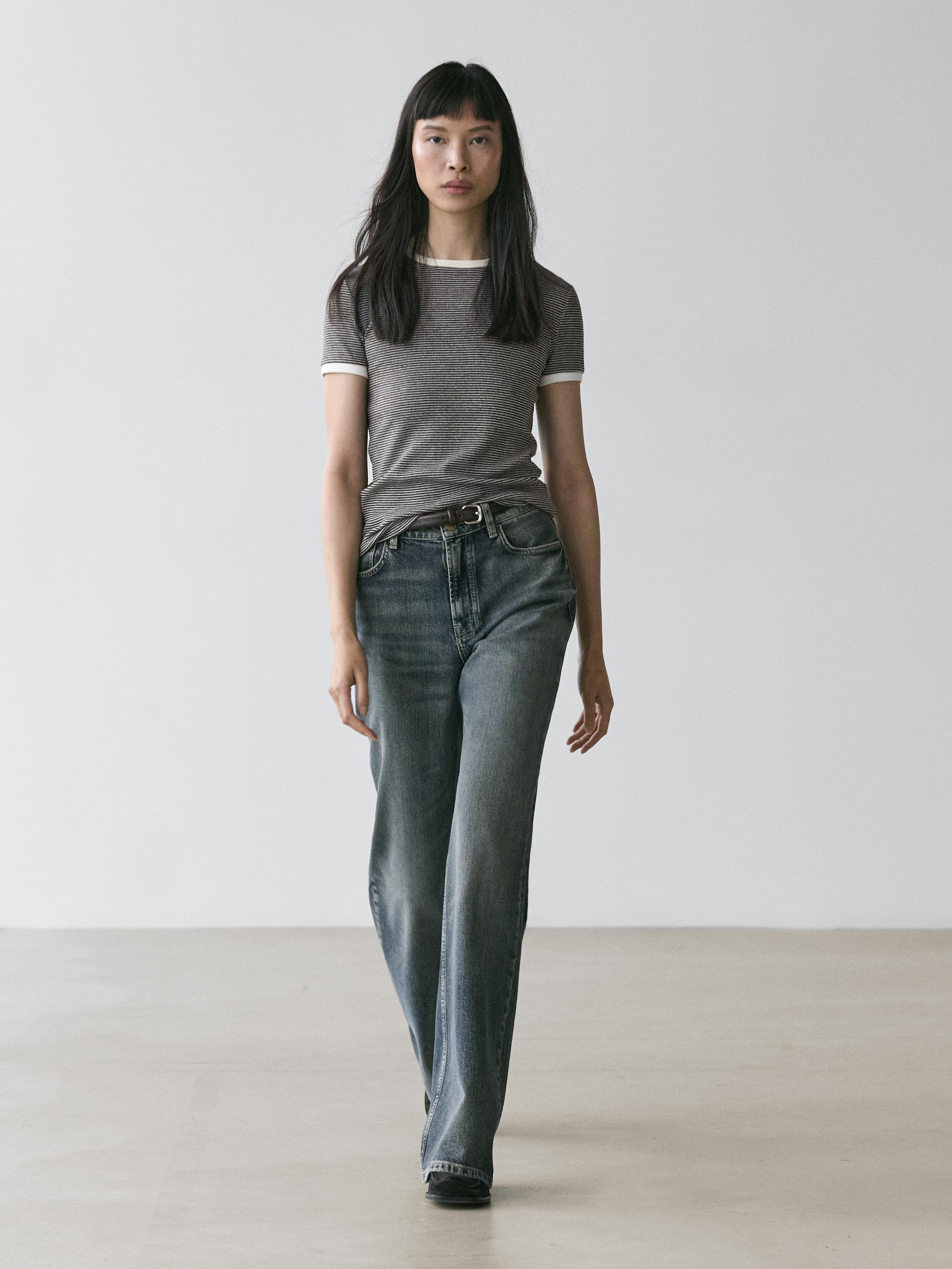 طقم تي شيرت رمادي مخطط بأكمام قصيرة وتطريز أبيض، وبنطلون جينز أزرق بقصة مستقيمة.