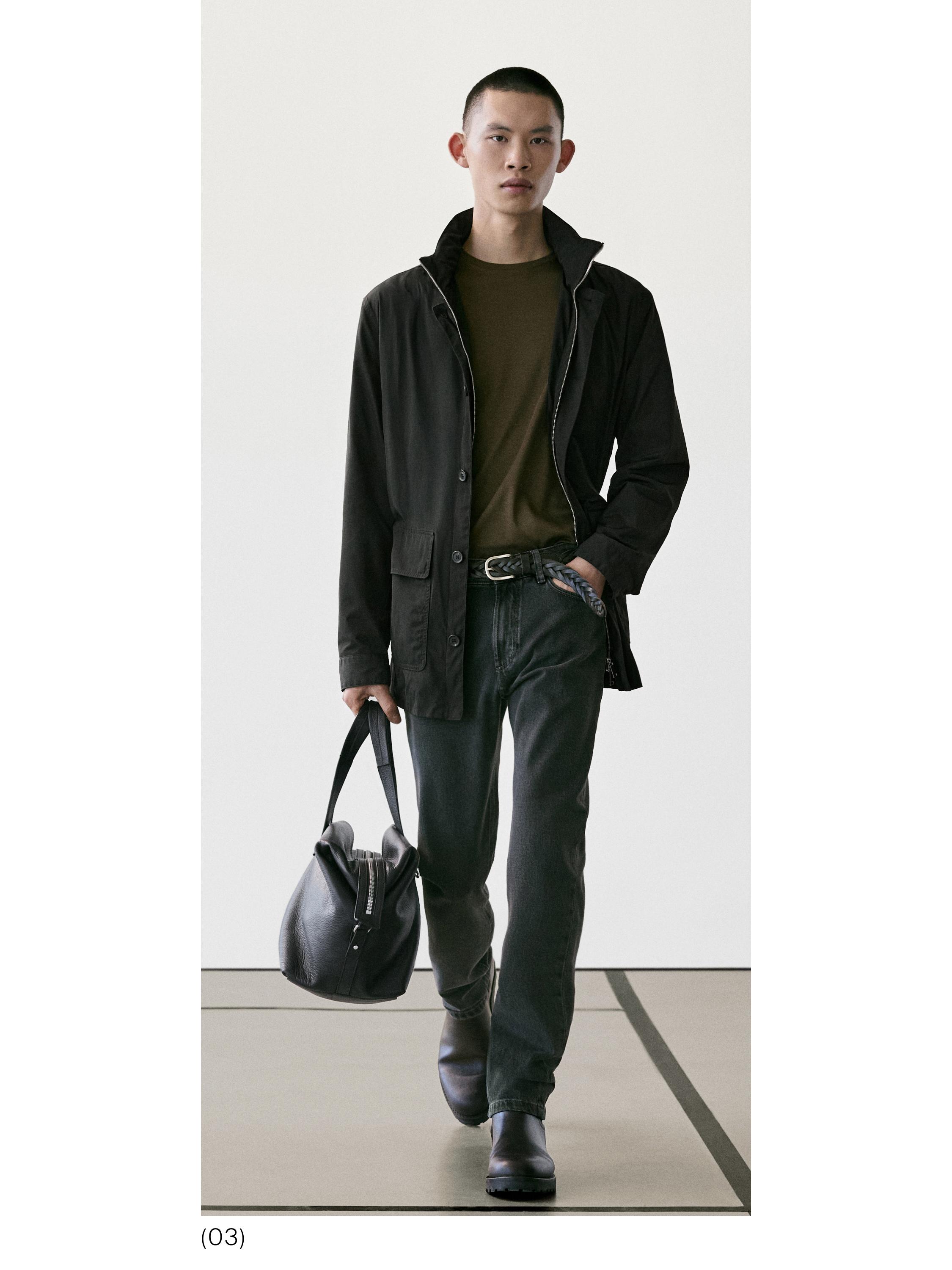 Conxunto composto por unha chaqueta negra con petos, unha camiseta marrón, pantalóns escuros e botas negras. Leva un bolso negro na man.