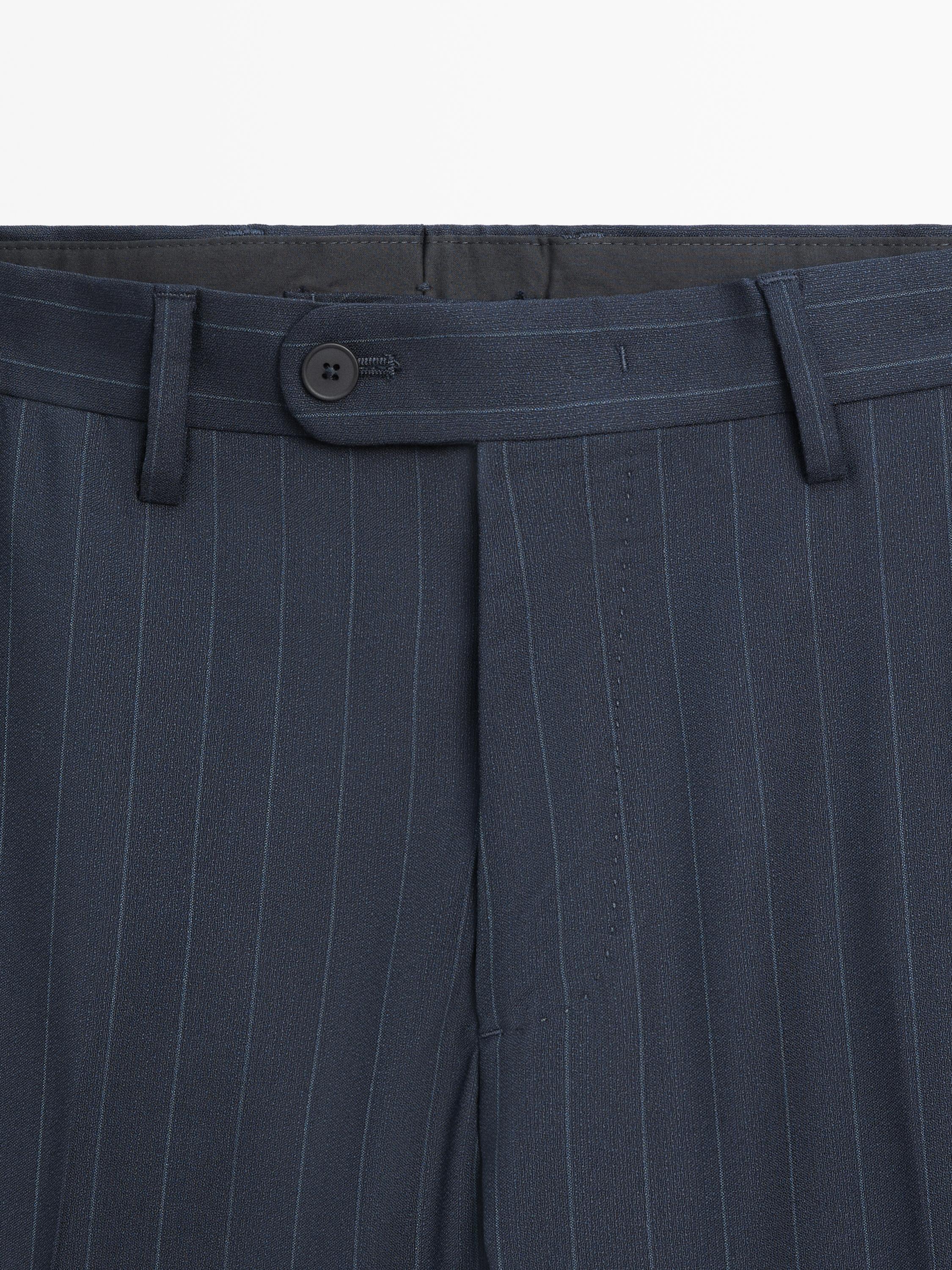 Mid-shot of the waist of navy blue pants with pinstripes, black button, and belt loops.