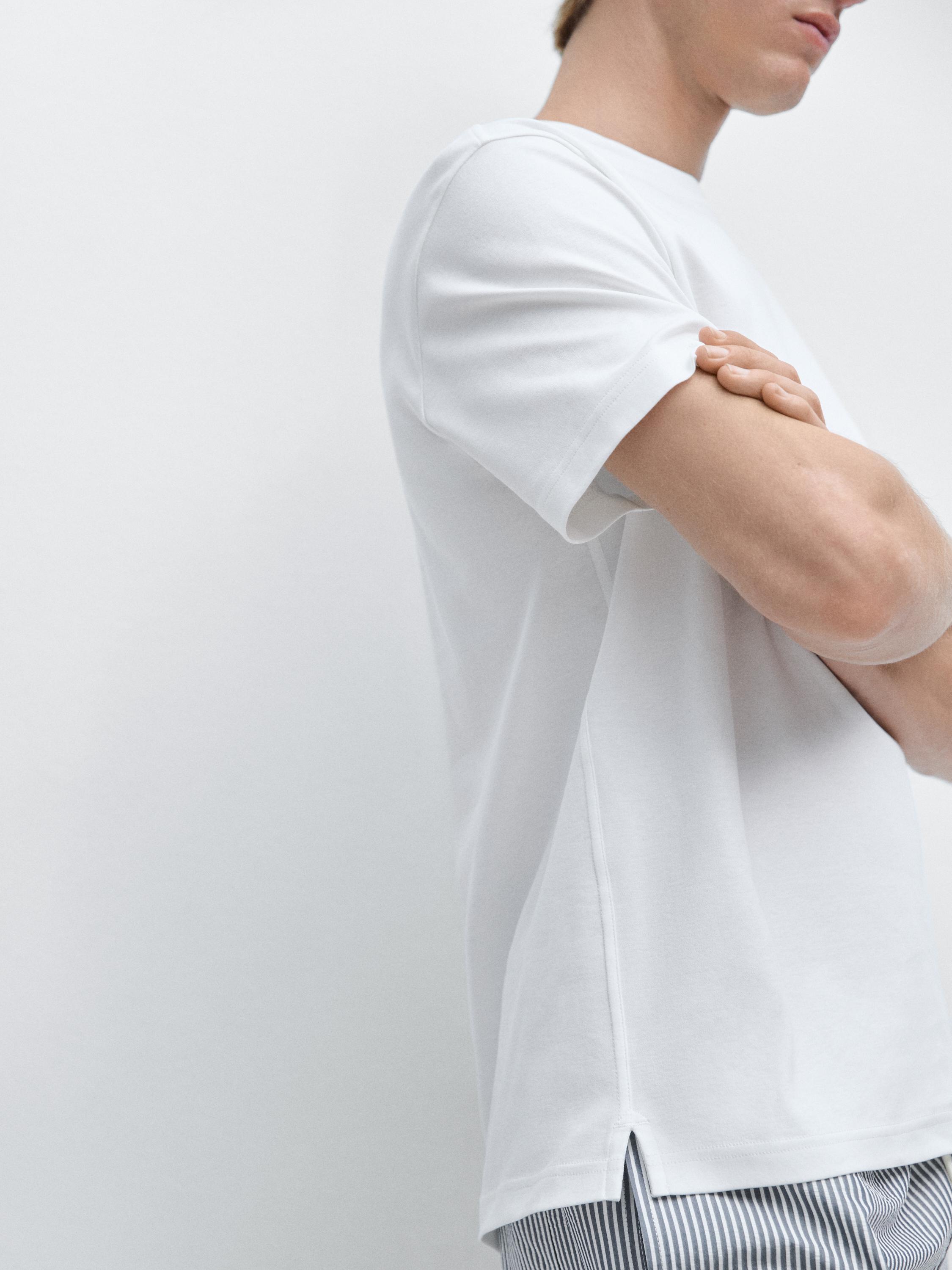 Kamiseta zuri mahuka motzaren plano ertaina, alboetan jositakoa eta marradun praka ikusgarriak dituena.