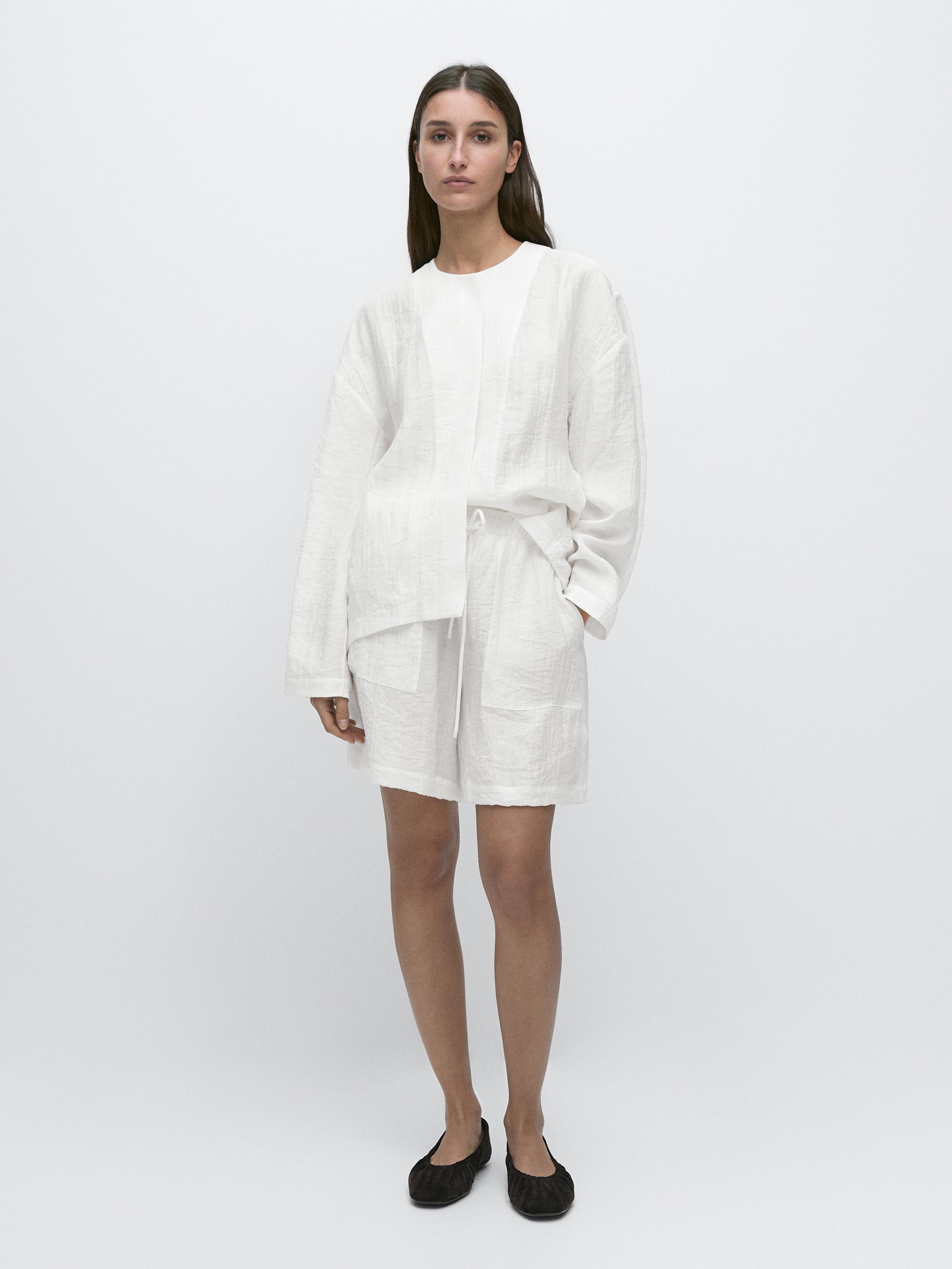 Conjunto de blusa y bermuda blanca con bolsillos laterales visibles, blusa de manga larga y cuello redondo.