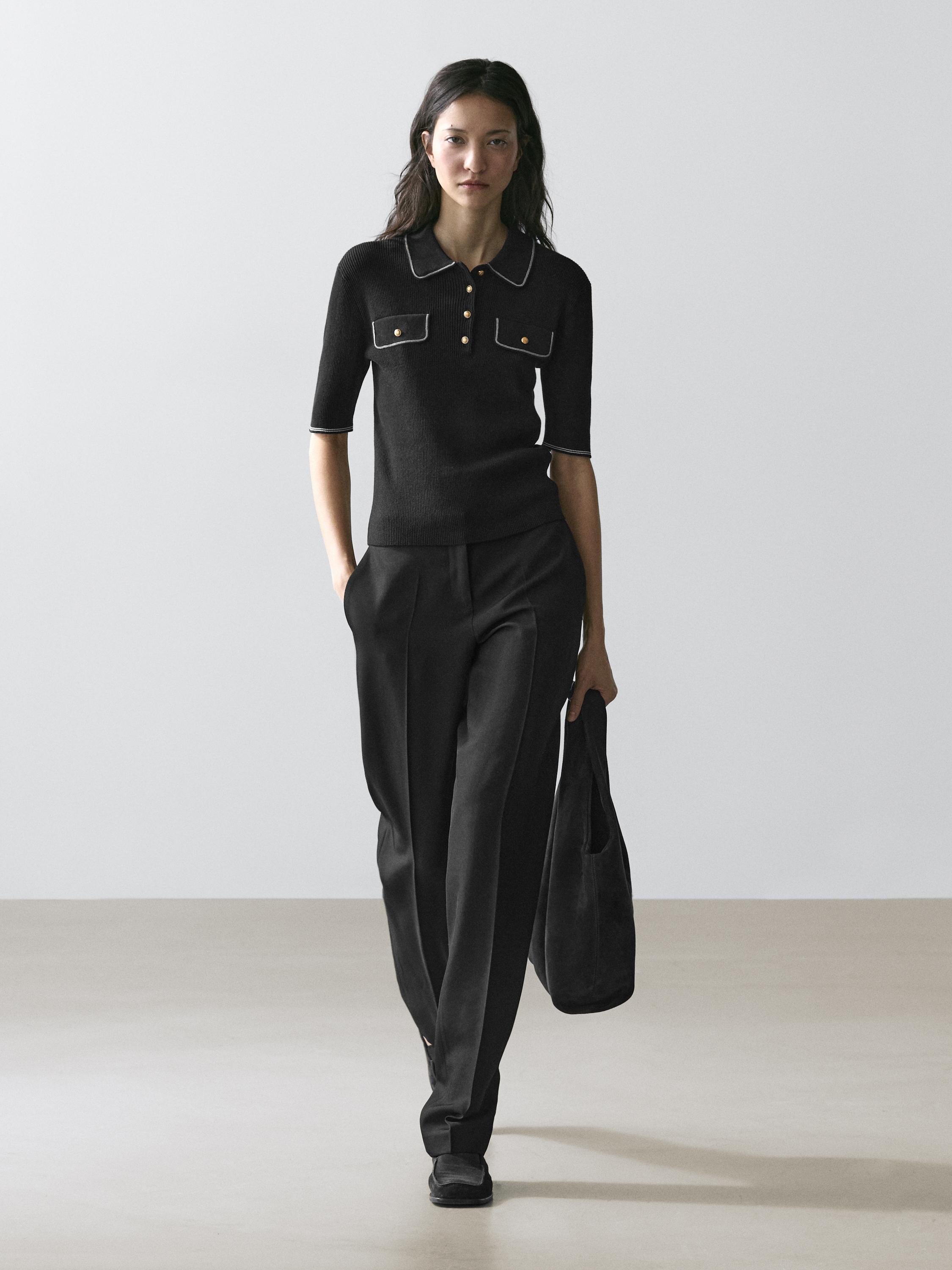 Conjunto de polo negro con bolsillos frontales y pantalones negros de pierna ancha.