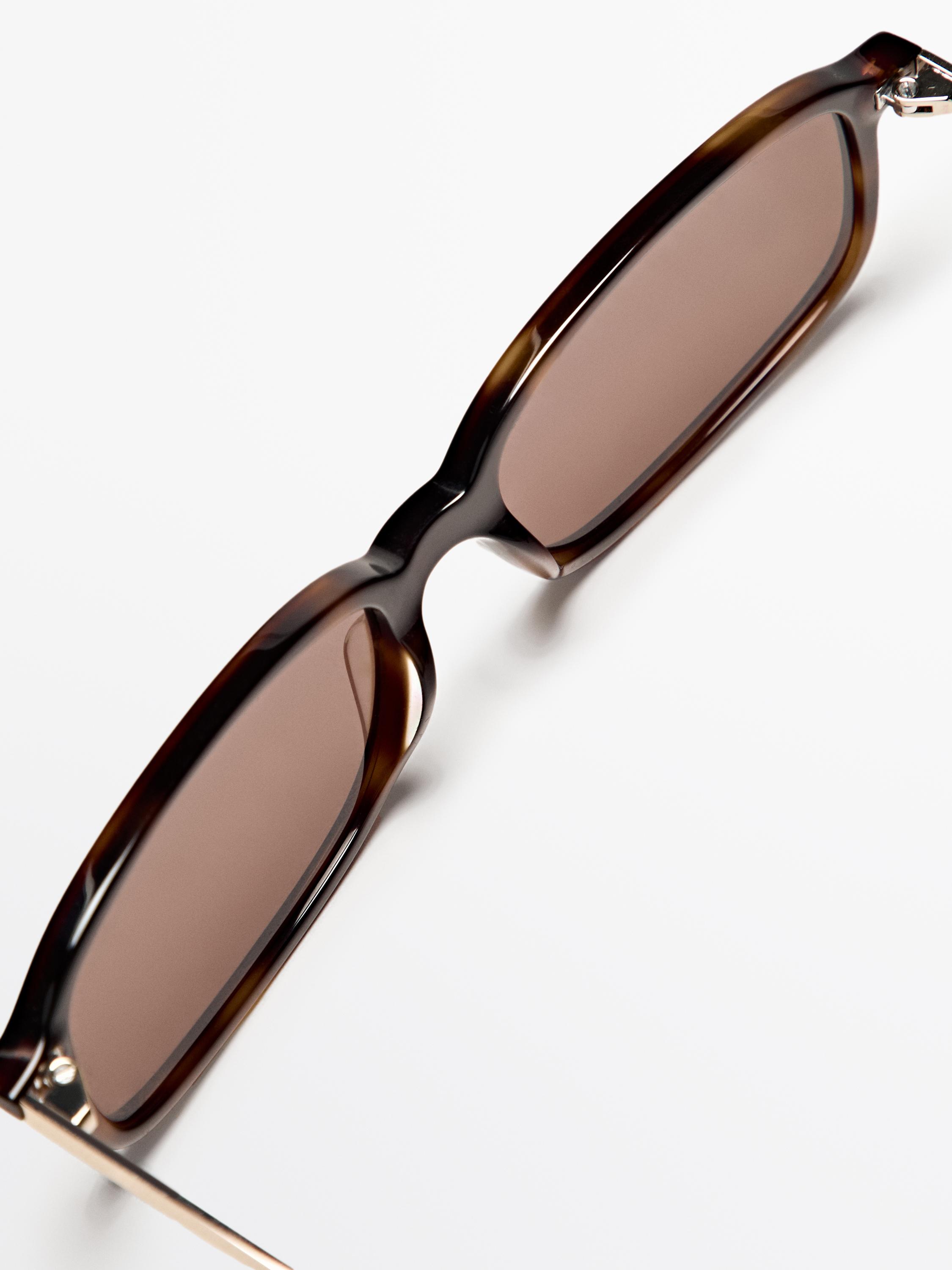 Eguzkitako betaurreko marroi pare baten lehen planoa, marko angeluzuzena eta hagaxka finak dituena. Kristalaren zabalera: 49 mm, zubia: 16 mm, hagaxka: 140 mm.