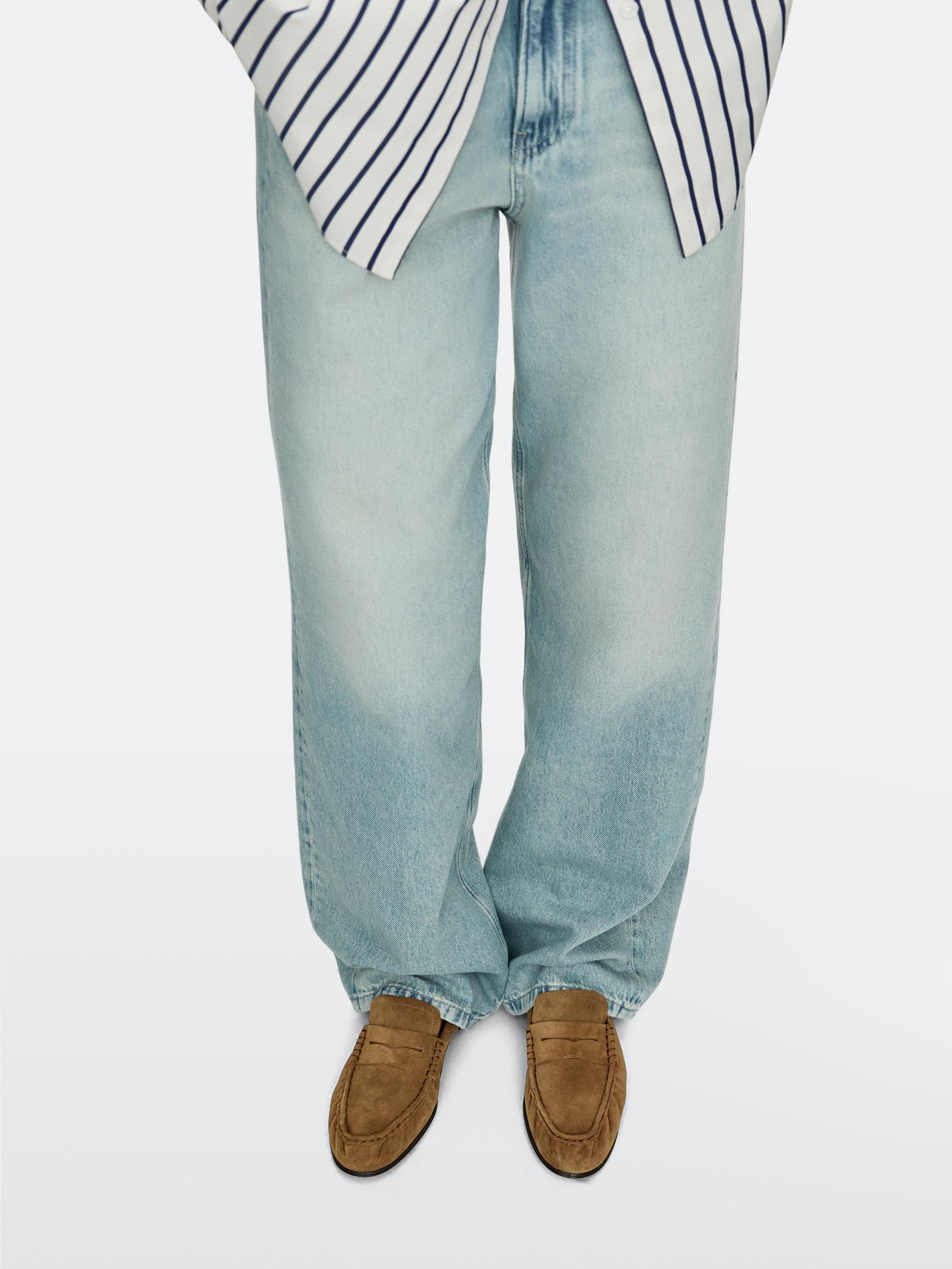 Halbnahe Aufnahme von kamelfarbenen Loafern mit sichtbaren Nähten, kombiniert mit hellen Jeans und einem gestreiften Hemd.