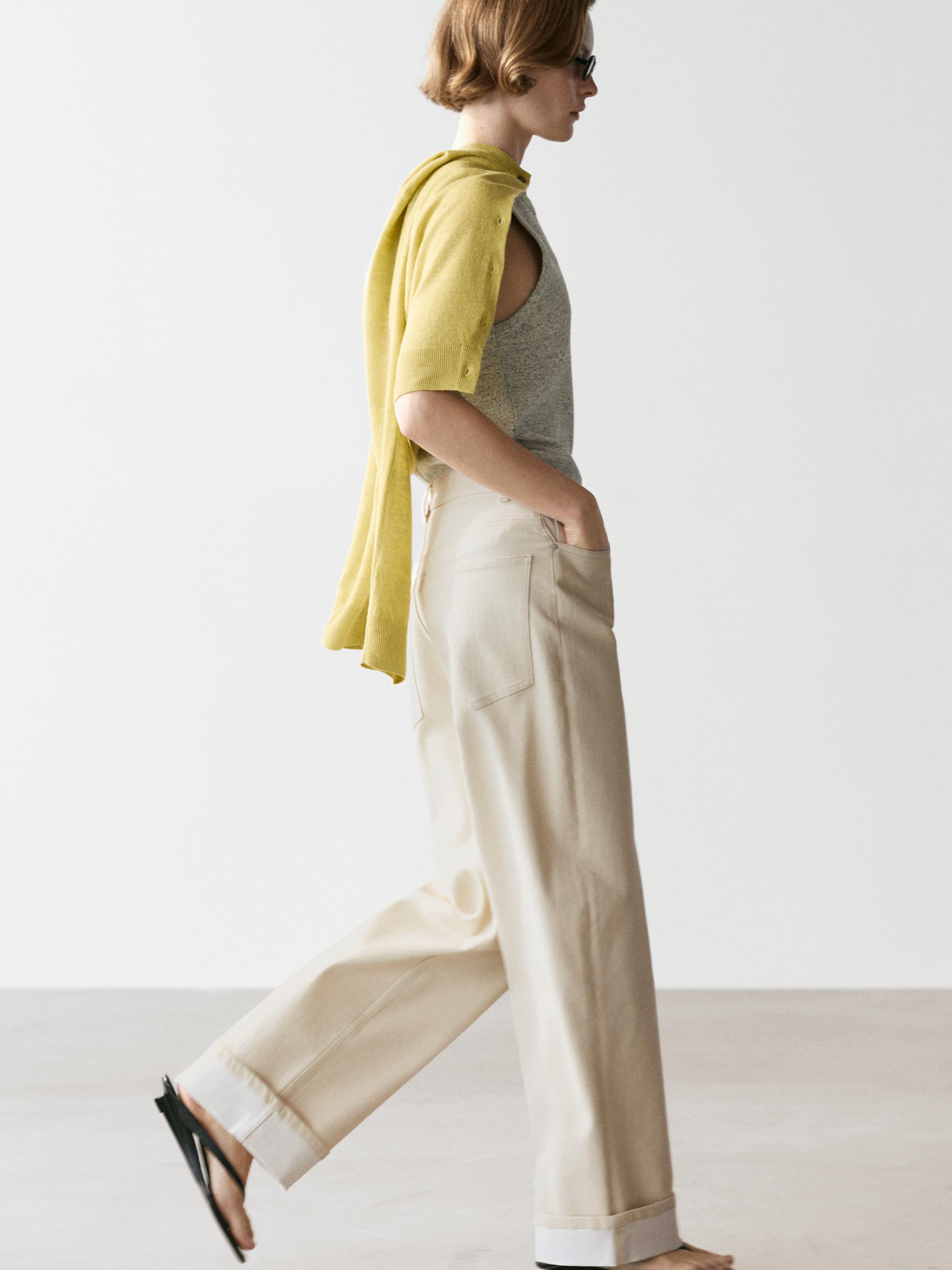 Limettenfarbenes Oversize-Cardigan-Set, graues ärmelloses T-Shirt und beige Hose mit Seitentaschen.