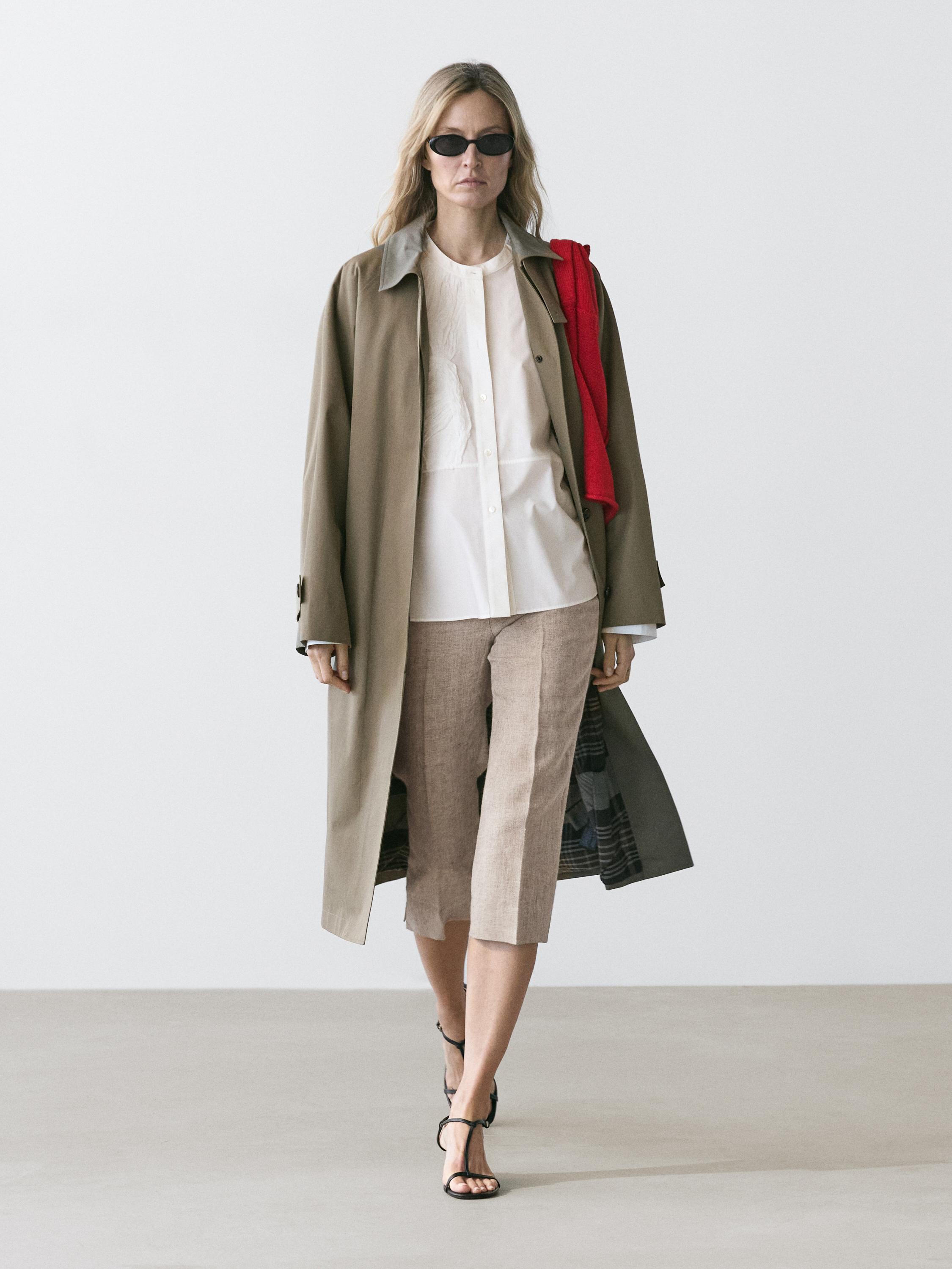 Beyaz gömlek, uzun bej palto, bej şort ve siyah sandalet kombini.