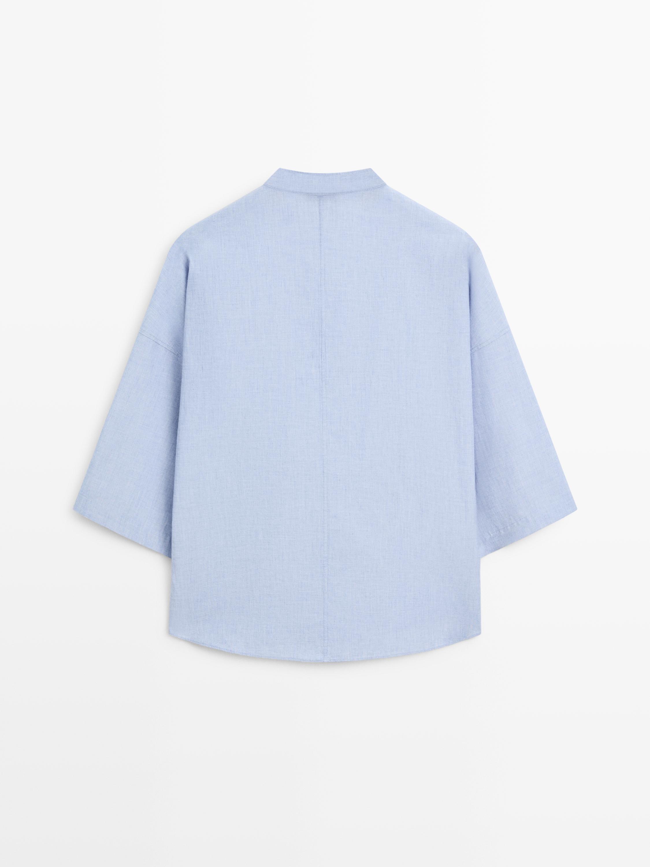 Widok z tyłu luźnej bluzki z niebieskiego denimu z kołnierzykiem typu mao i szerokimi rękawami.