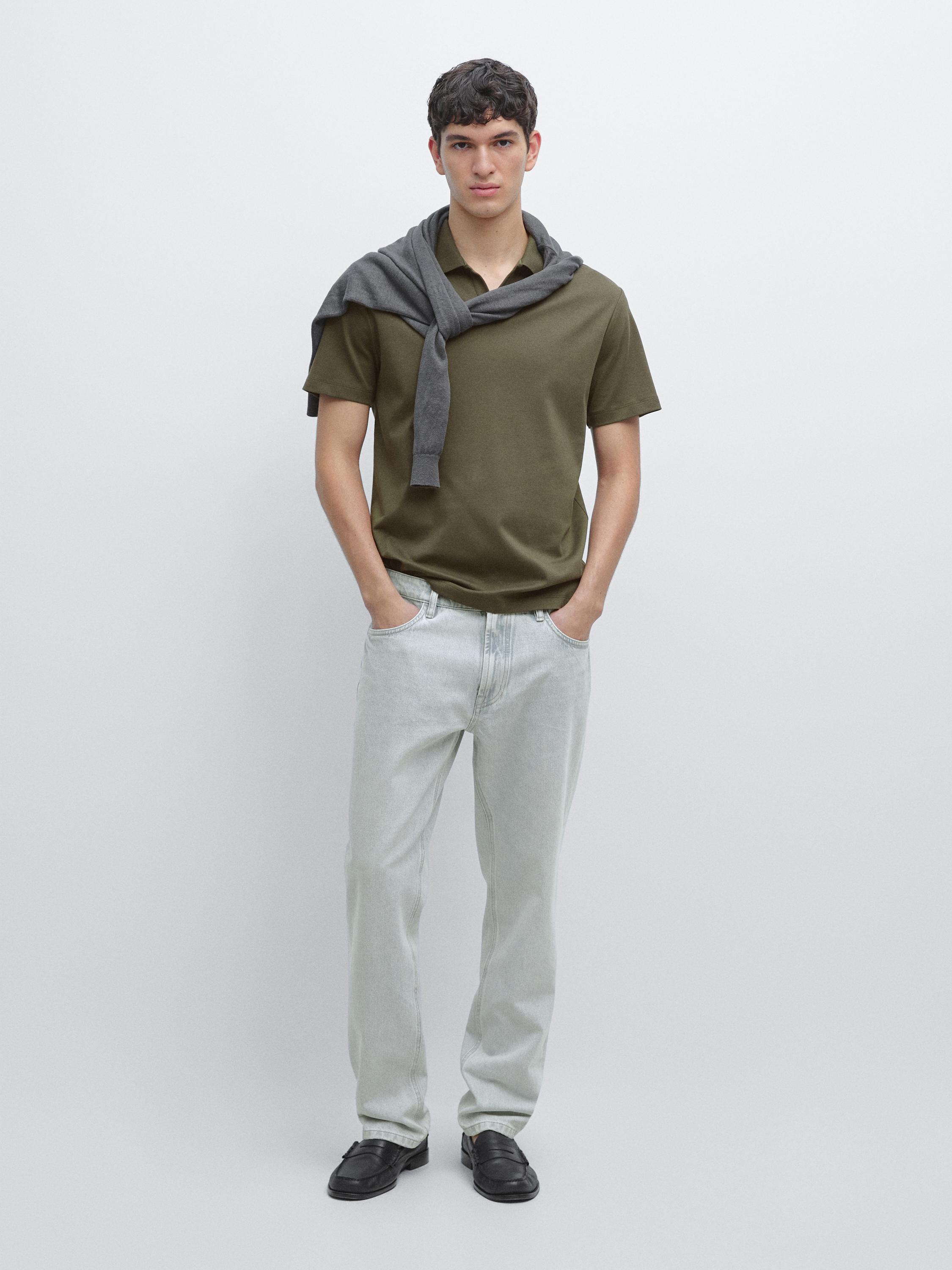 Bộ áo polo kaki tay ngắn, quần jeans sáng màu và giày đen. Áo len xám buộc quanh cổ.