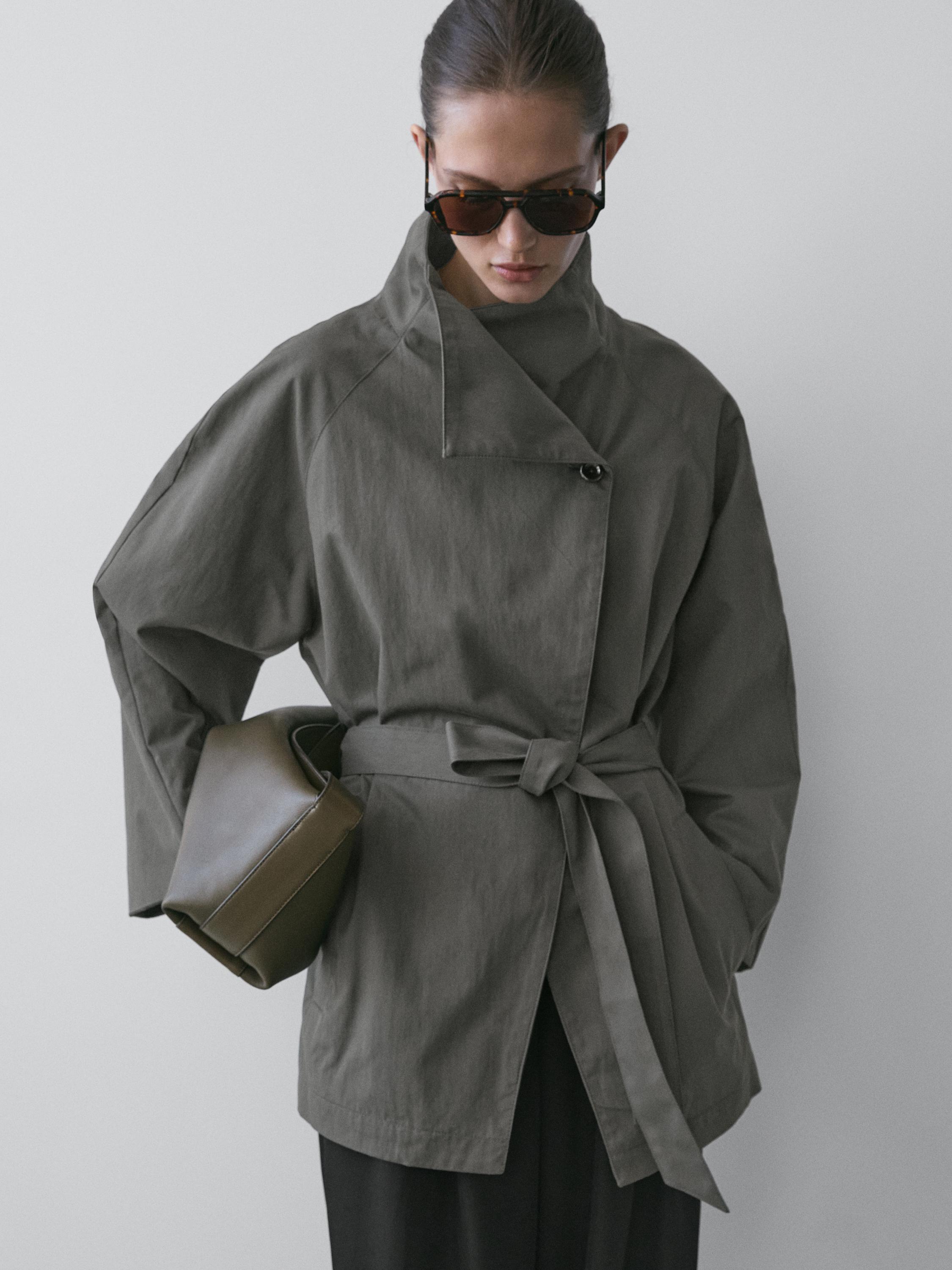 Medium shot of a mid-blue trench coat with a belt and an asymmetrical closure.