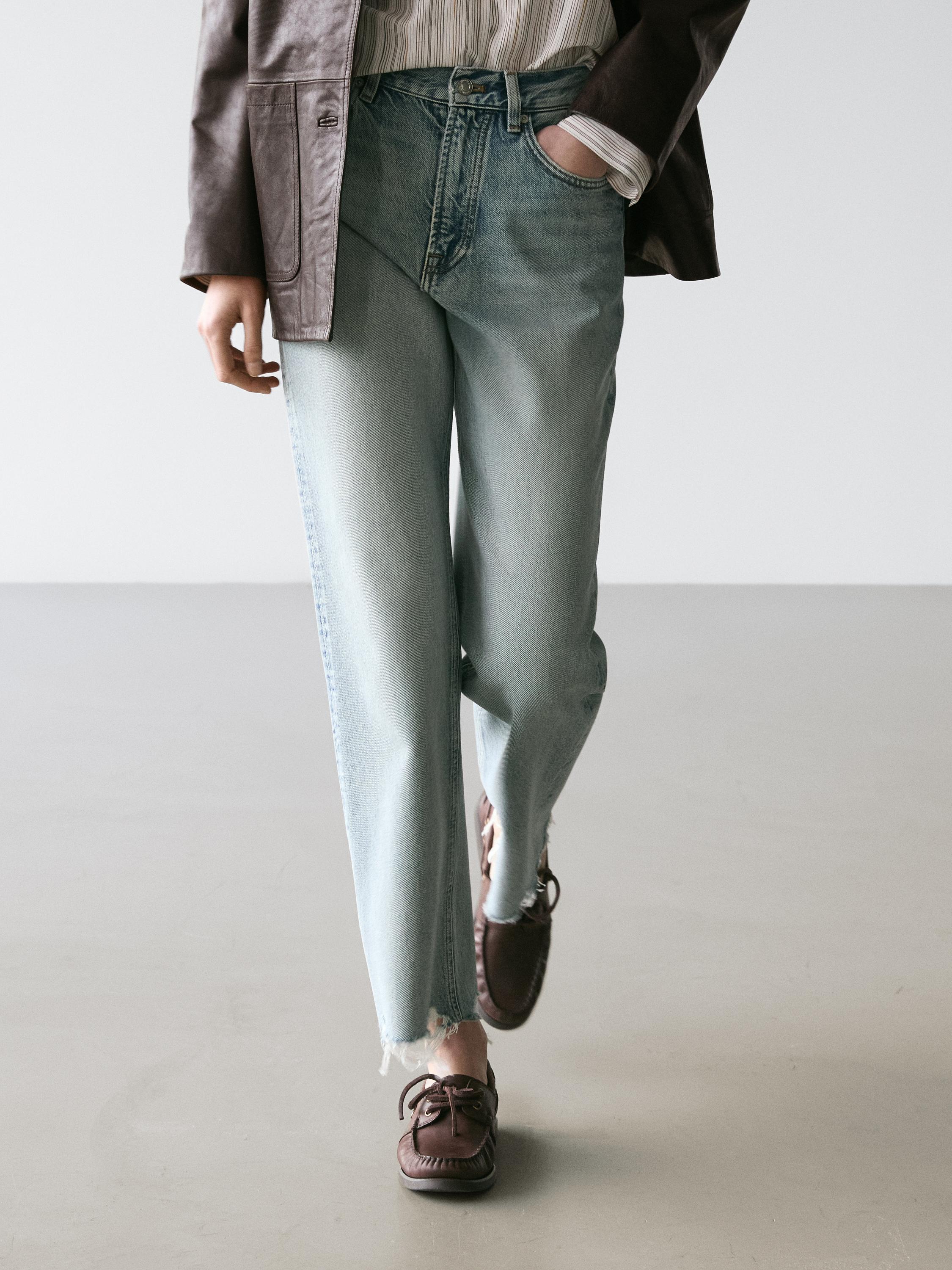 Plan moyen d'un jean bleu clair taille haute, coupe droite, avec des poches avant et des bas effilochés.