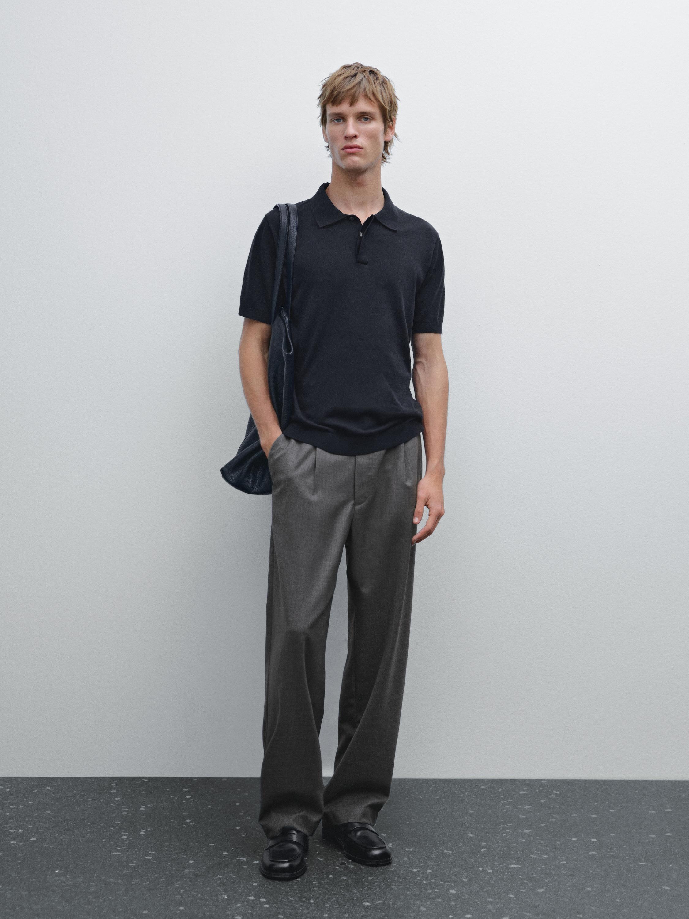 Ensemble polo noir et pantalon gris ample avec chaussures noires.