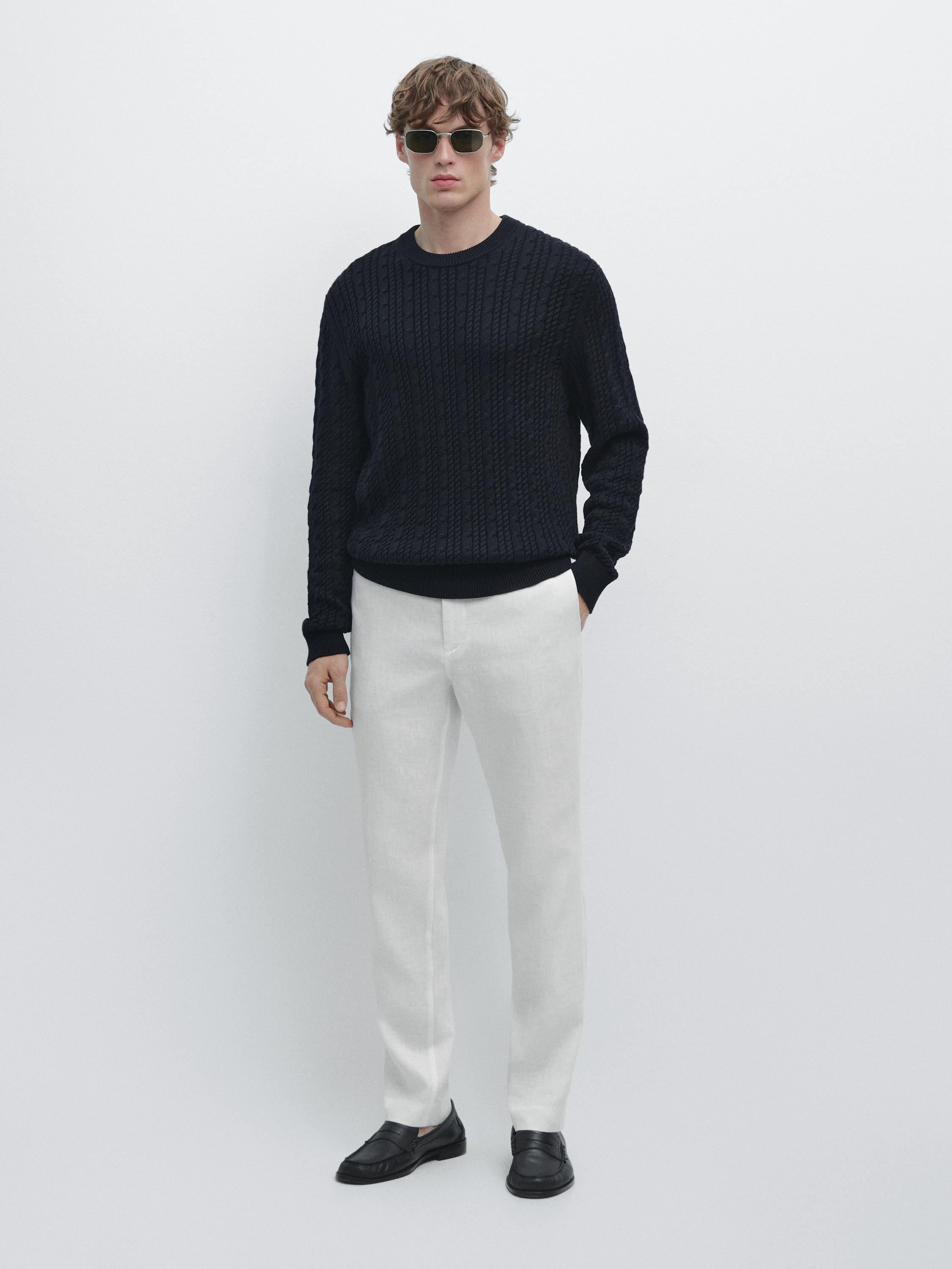 White tapered fit pants set with side pockets and a black cable-knit sweater.